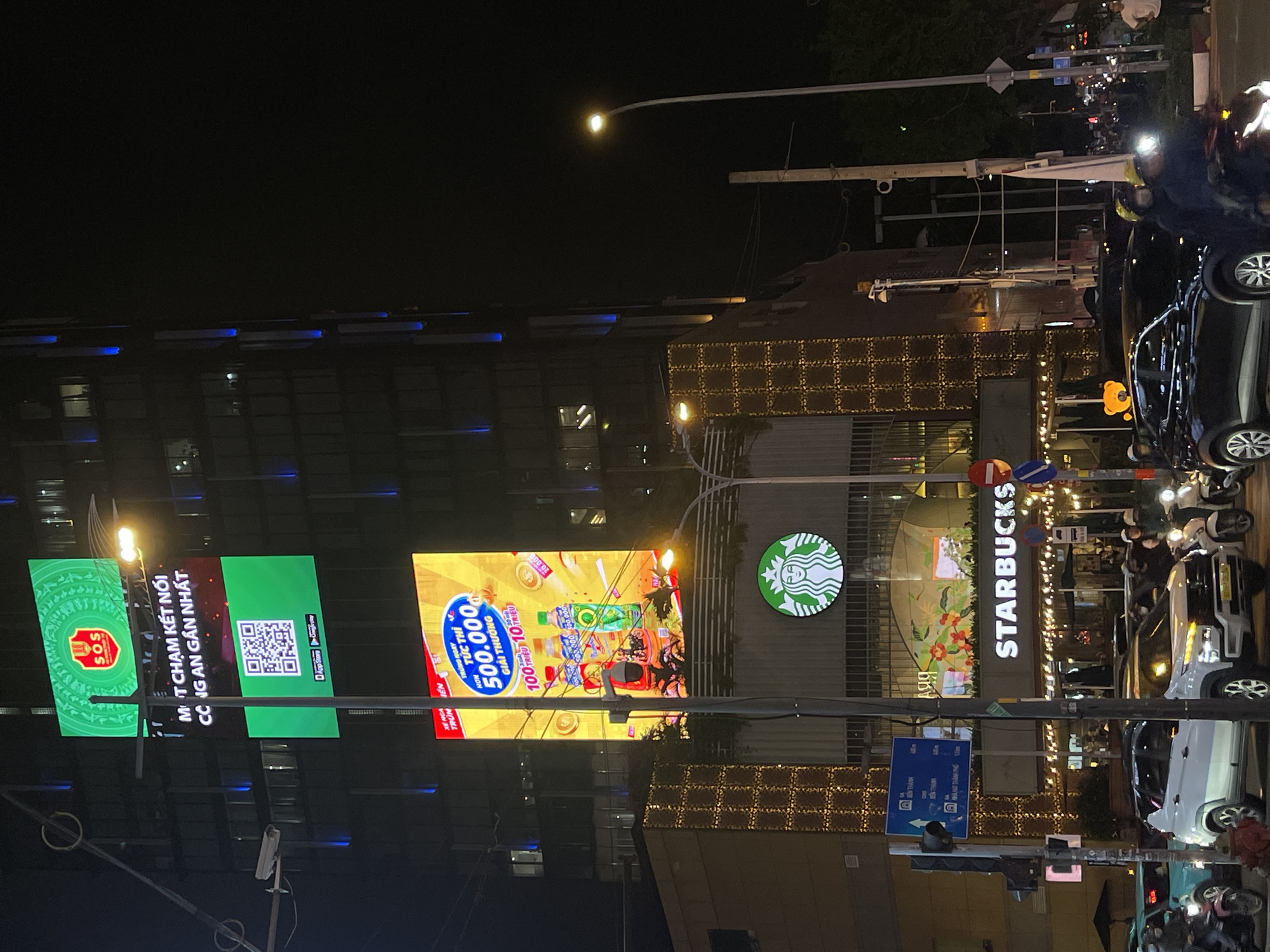 Night traffic flows past illuminated Starbucks in Thủ Đức