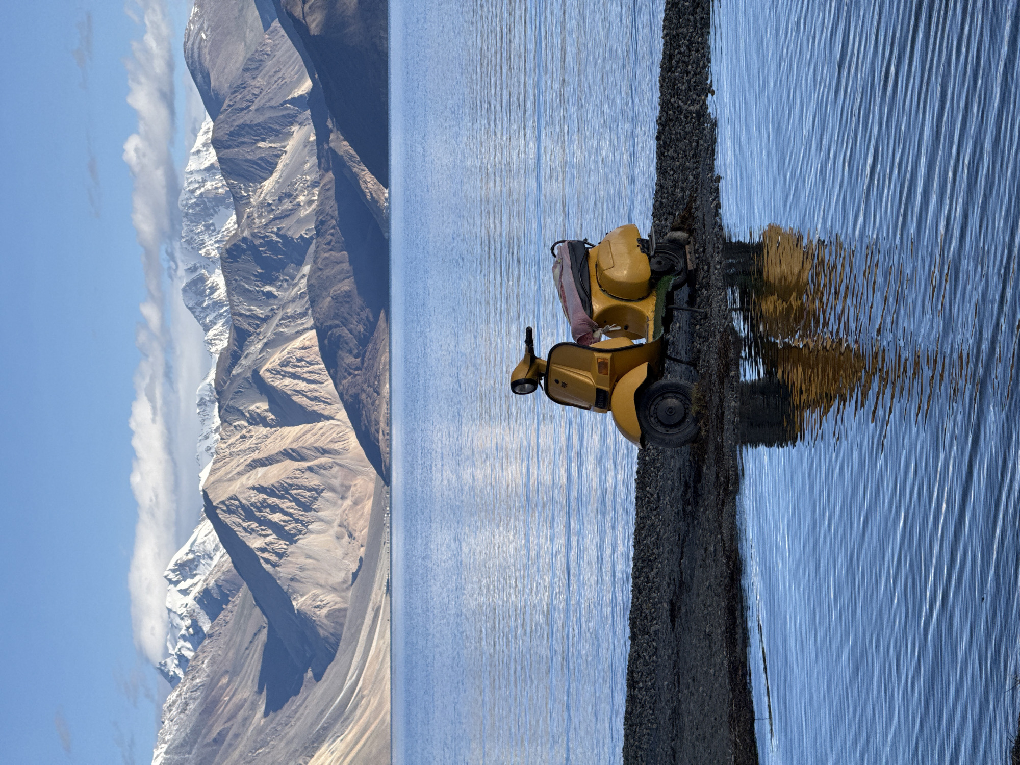 Yellow scooter parked by a calm Ladakhi mountain lake