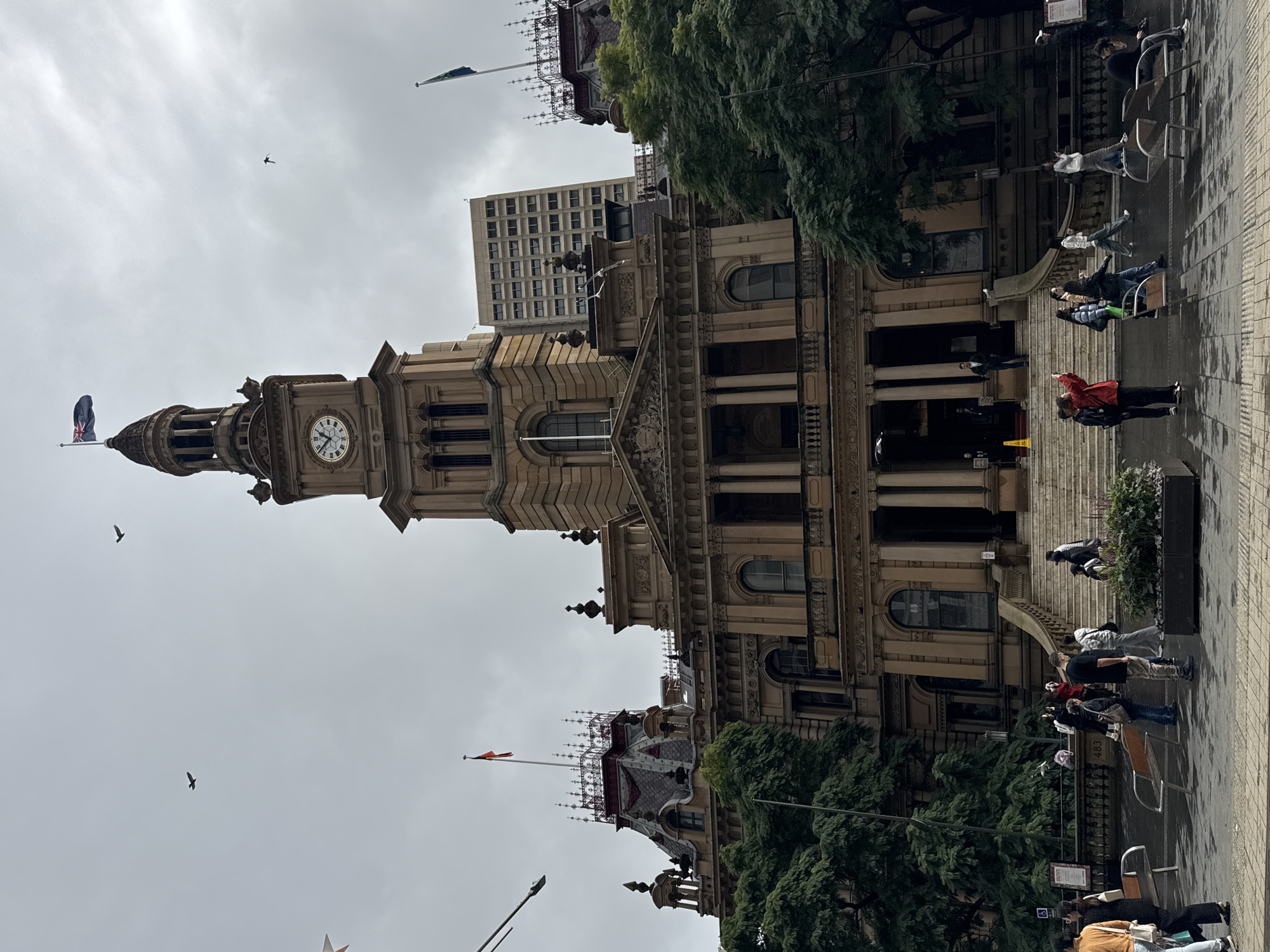 Ornate clock tower building under overcast skies, birds in flight
