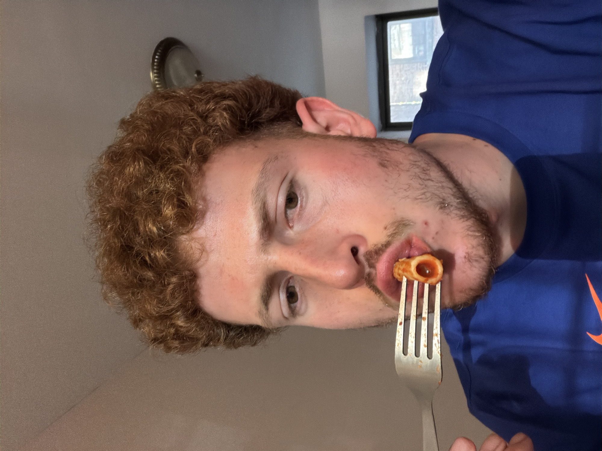 Man eats pasta in NYC apartment with basketball poster