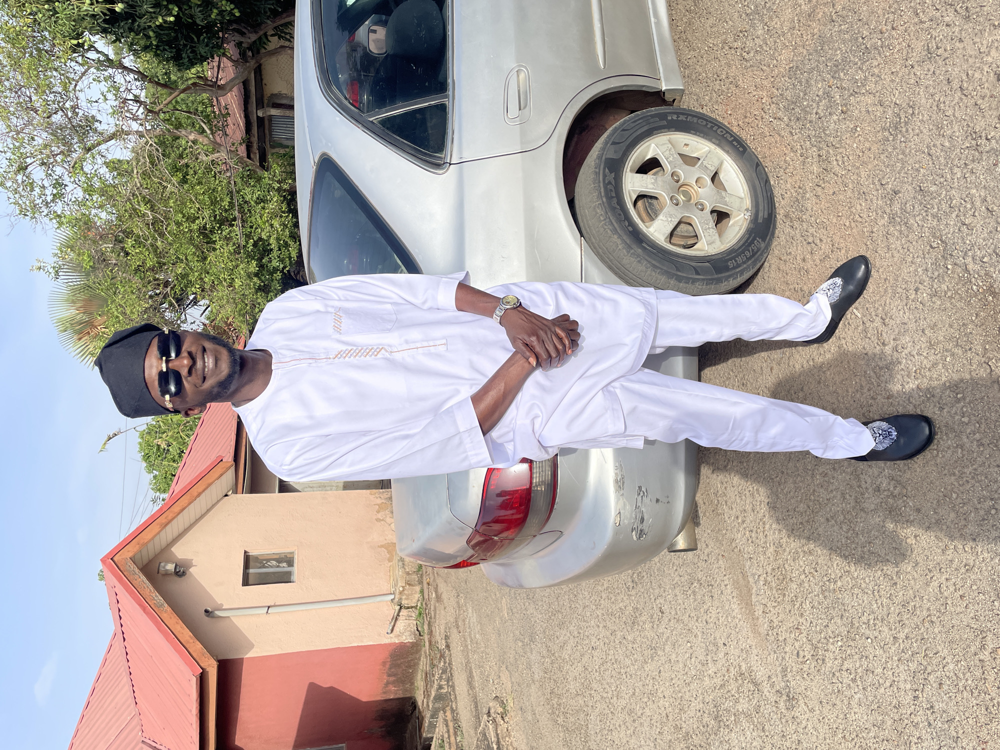 Man in traditional dress poses with silver car