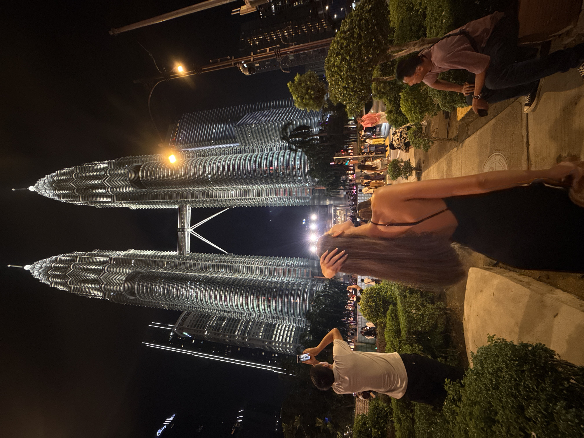 Evening crowds photograph illuminated Petronas Towers in Kuala Lumpur