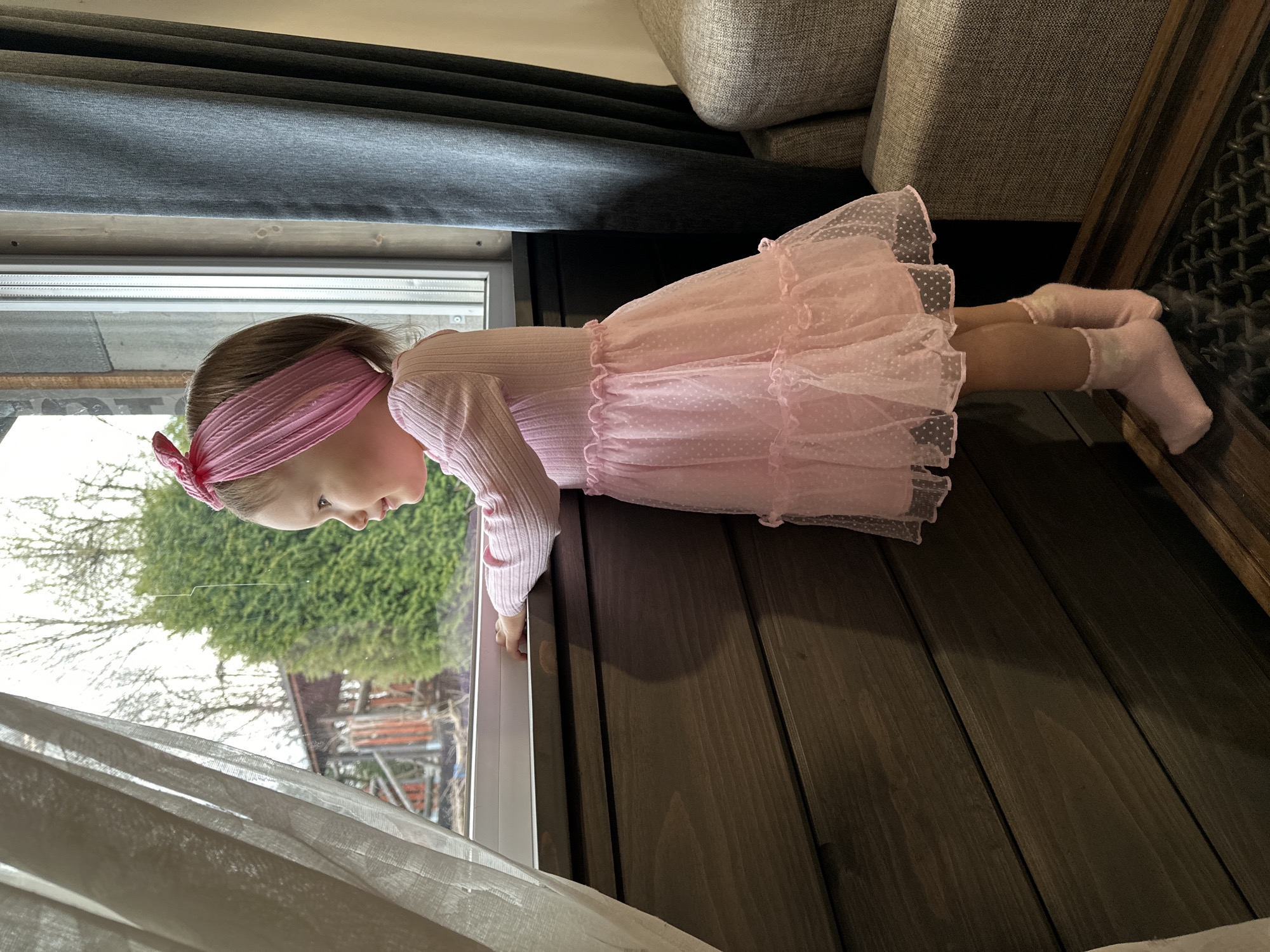 Young girl in pink dress plays by window in Wisła
