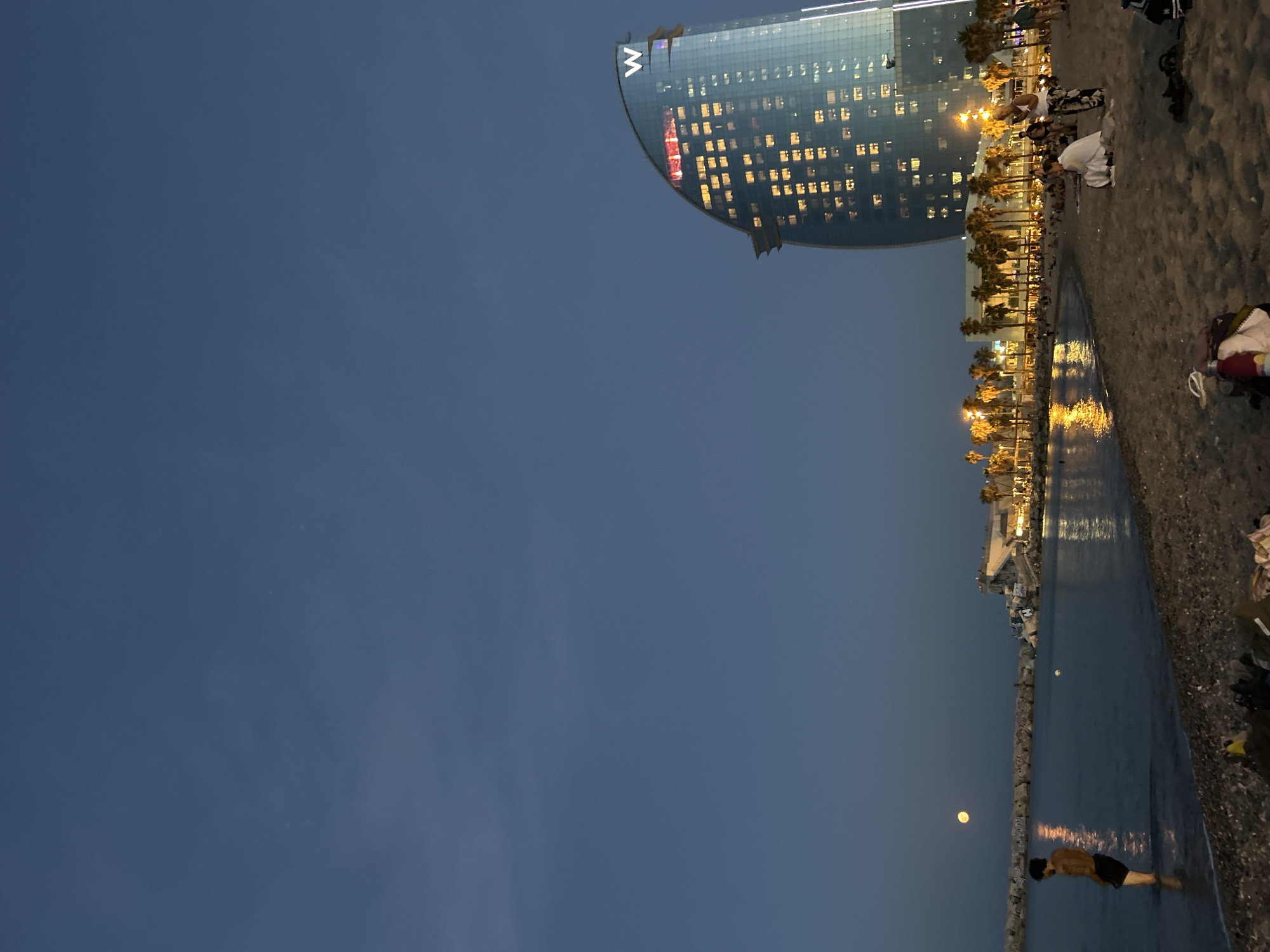Full moon rises over Barcelona's calm waterfront at twilight