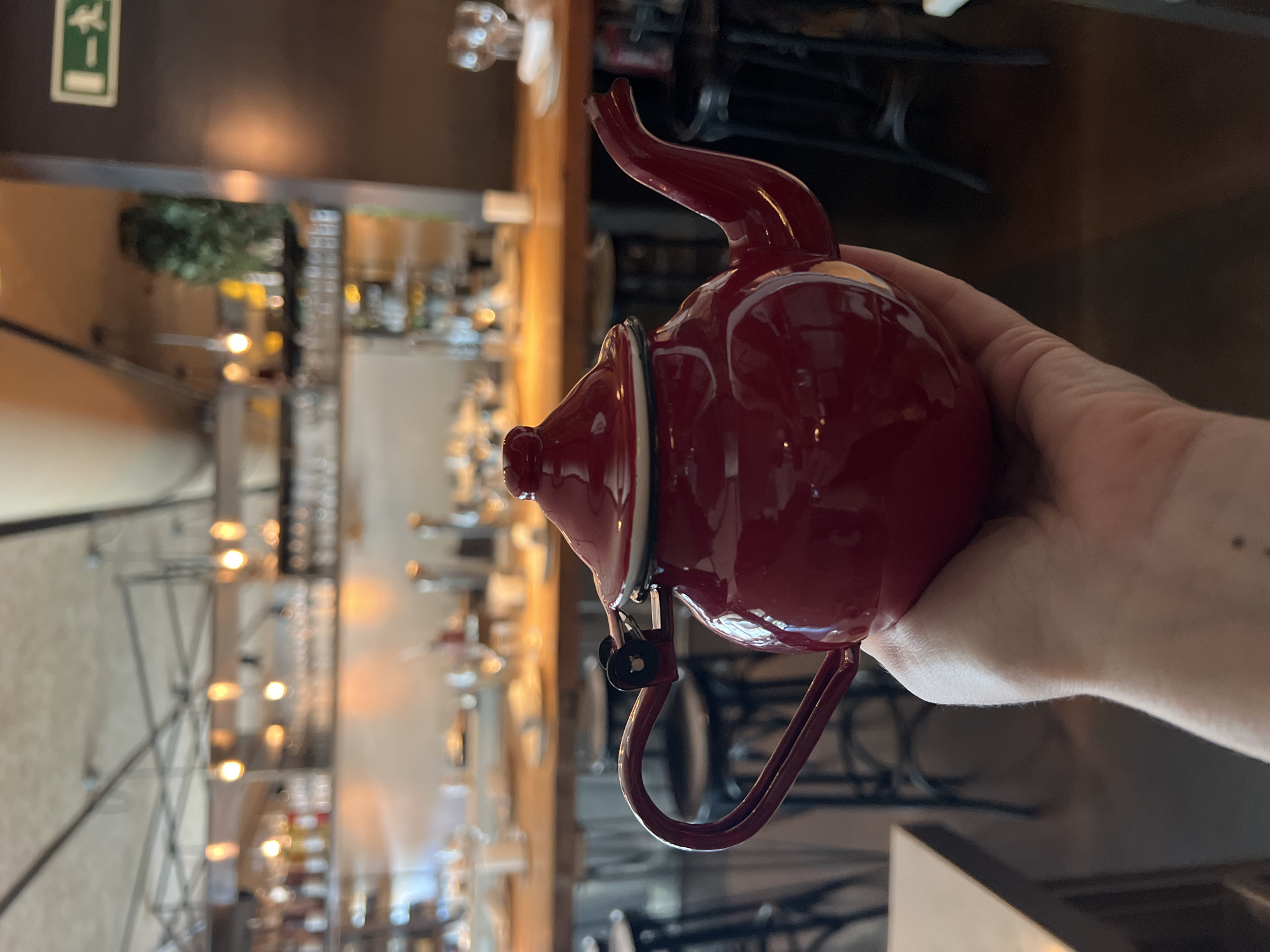 Dark red teapot held up against a Barcelona bar backdrop