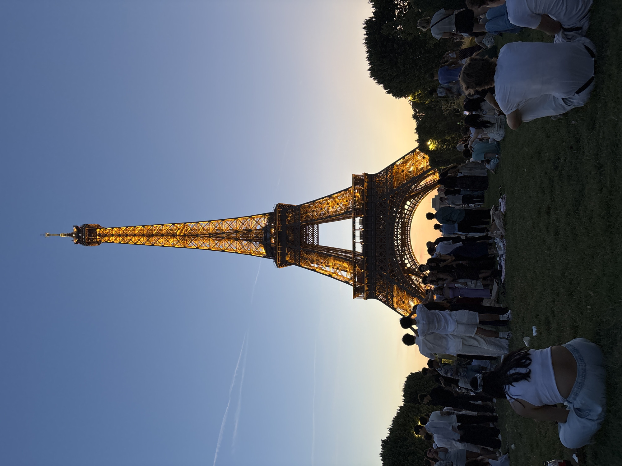 Eiffel Tower glows at dusk as crowds gather on the lawn