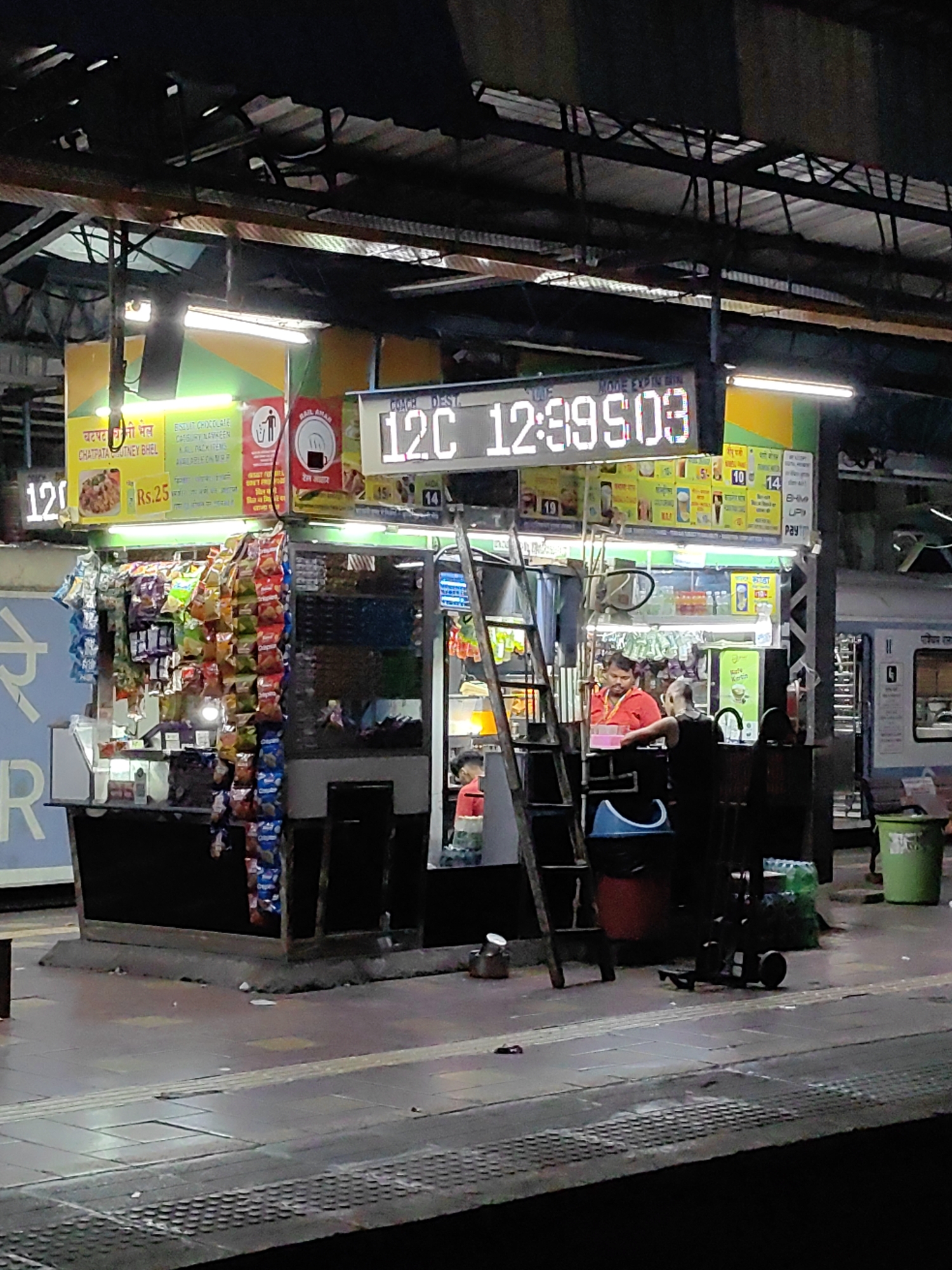 Late-night Mumbai railway station: platform stall and moving train