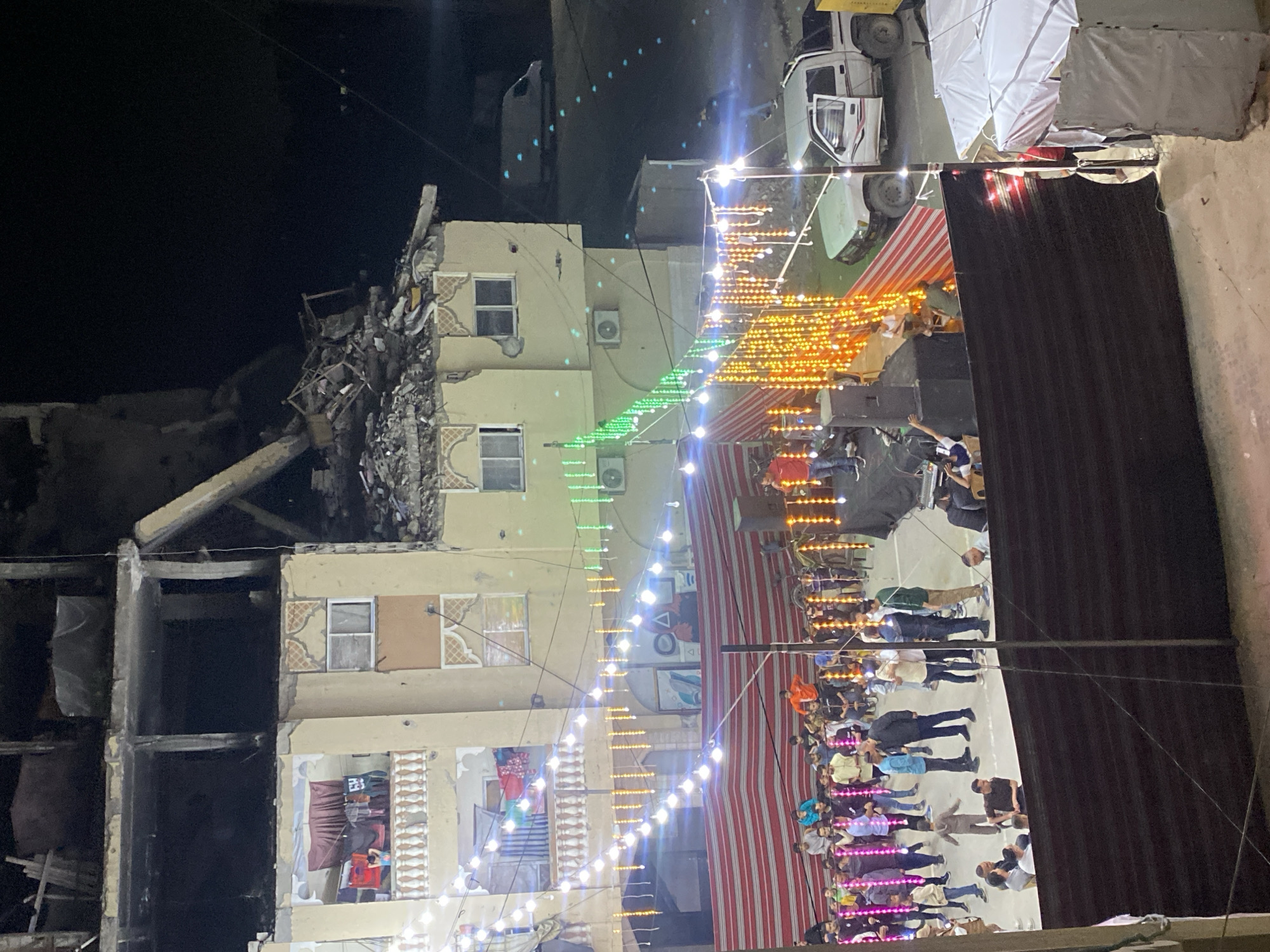 Nighttime gathering amid damaged buildings in Khan Yunis courtyard