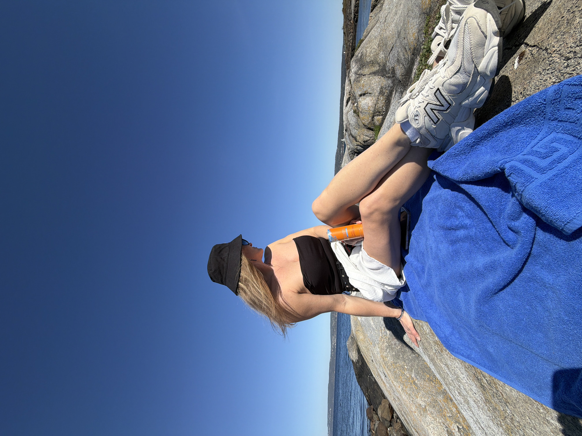 Person relaxes on Norwegian coast as sailboat drifts nearby