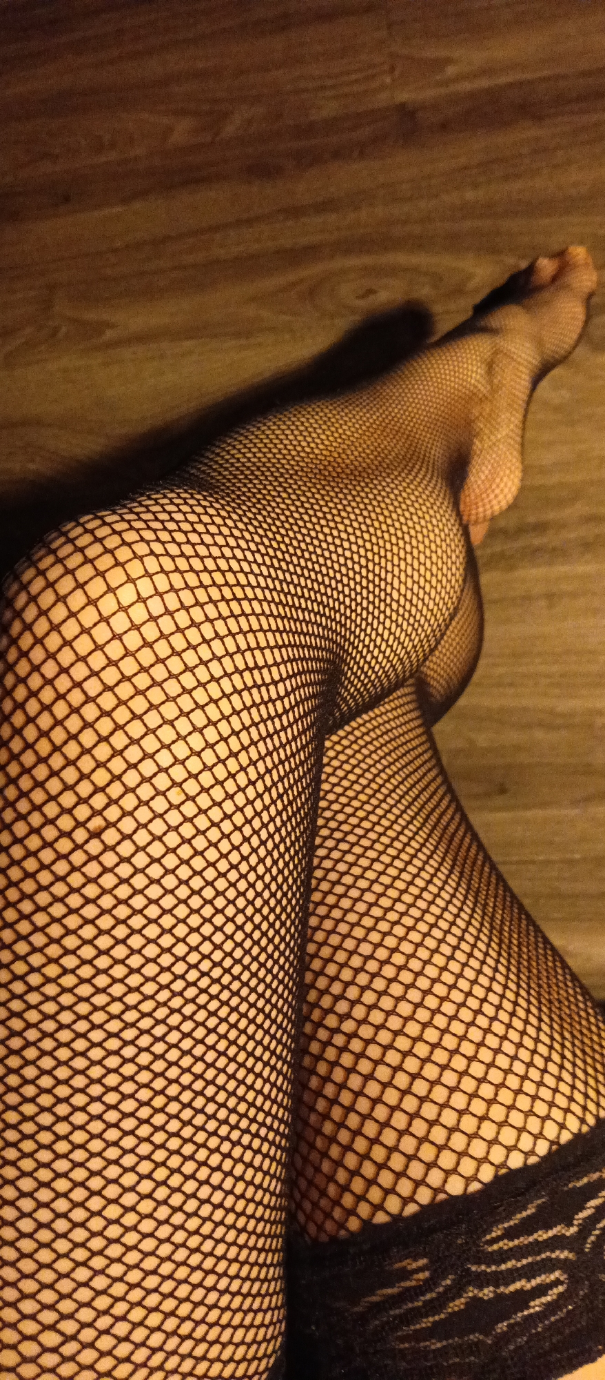 Person photographed in fishnet stockings, Christmas lights on wooden floor