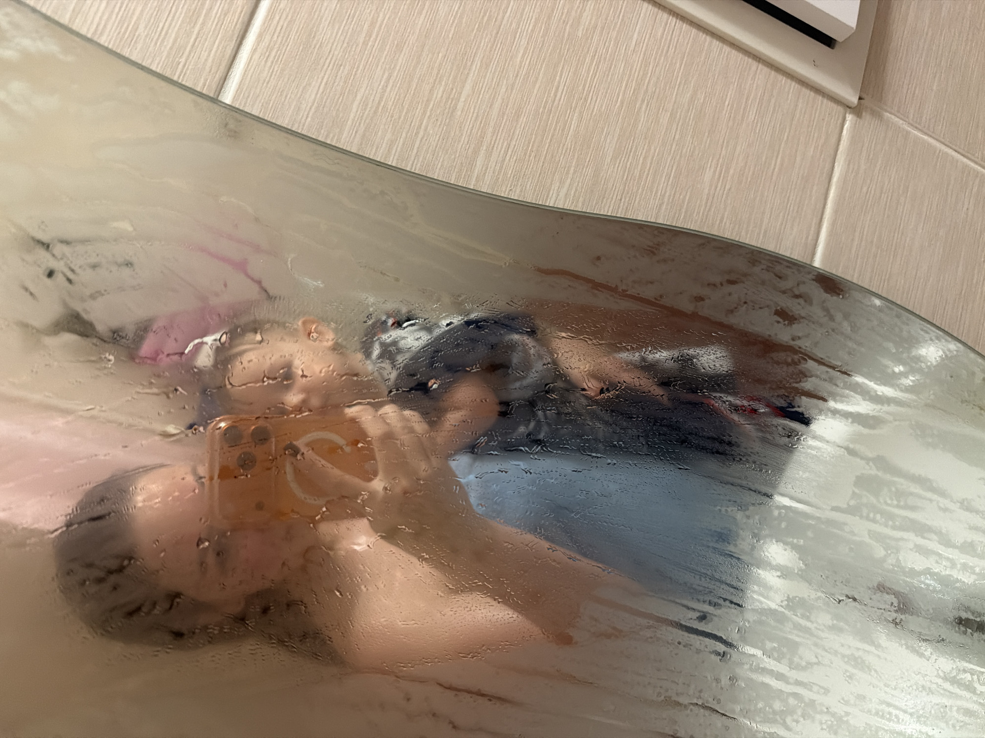 Selfie reflection captured through steamy shower door in Ufa