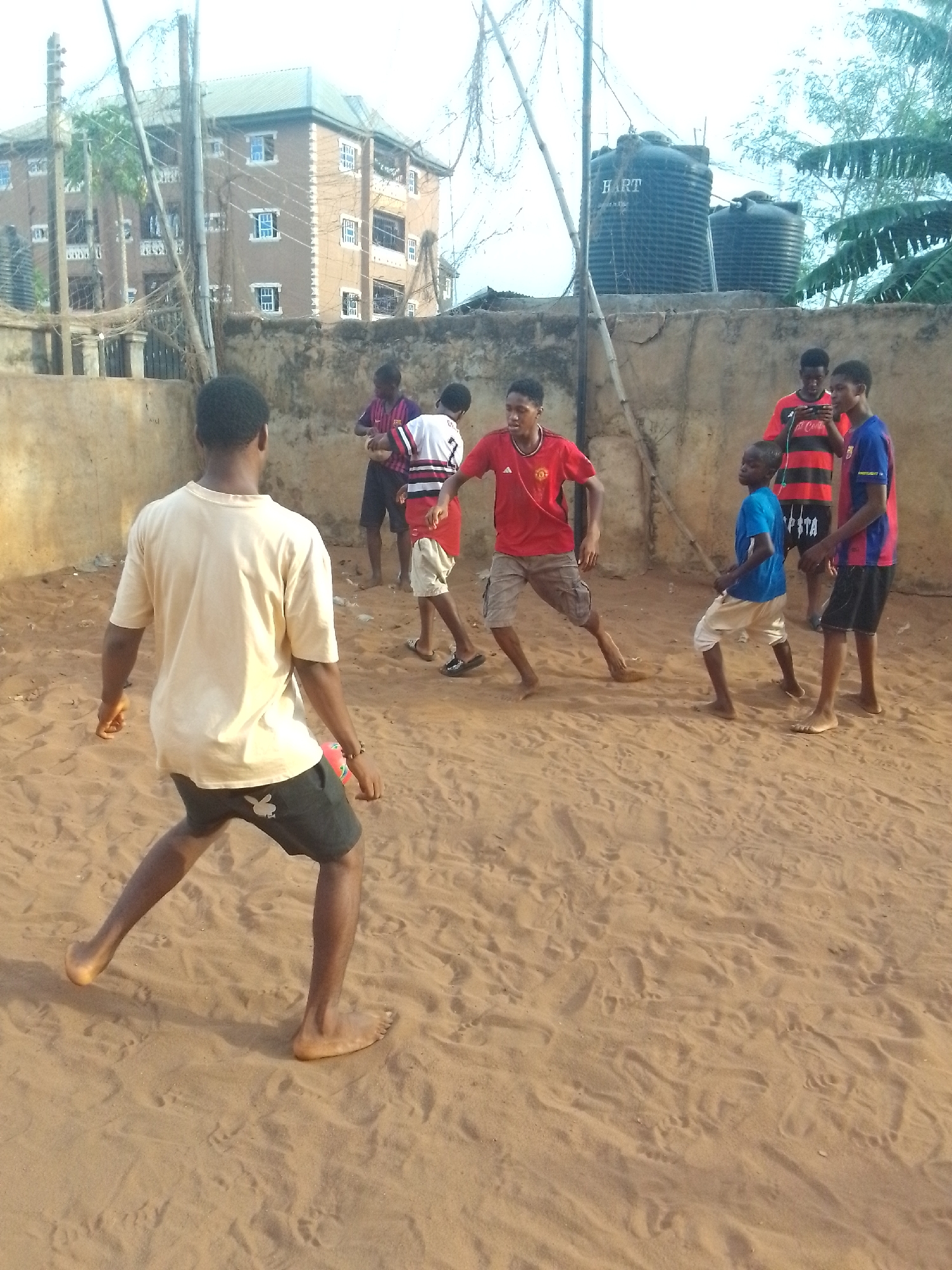 Young men play barefoot soccer on dirt field