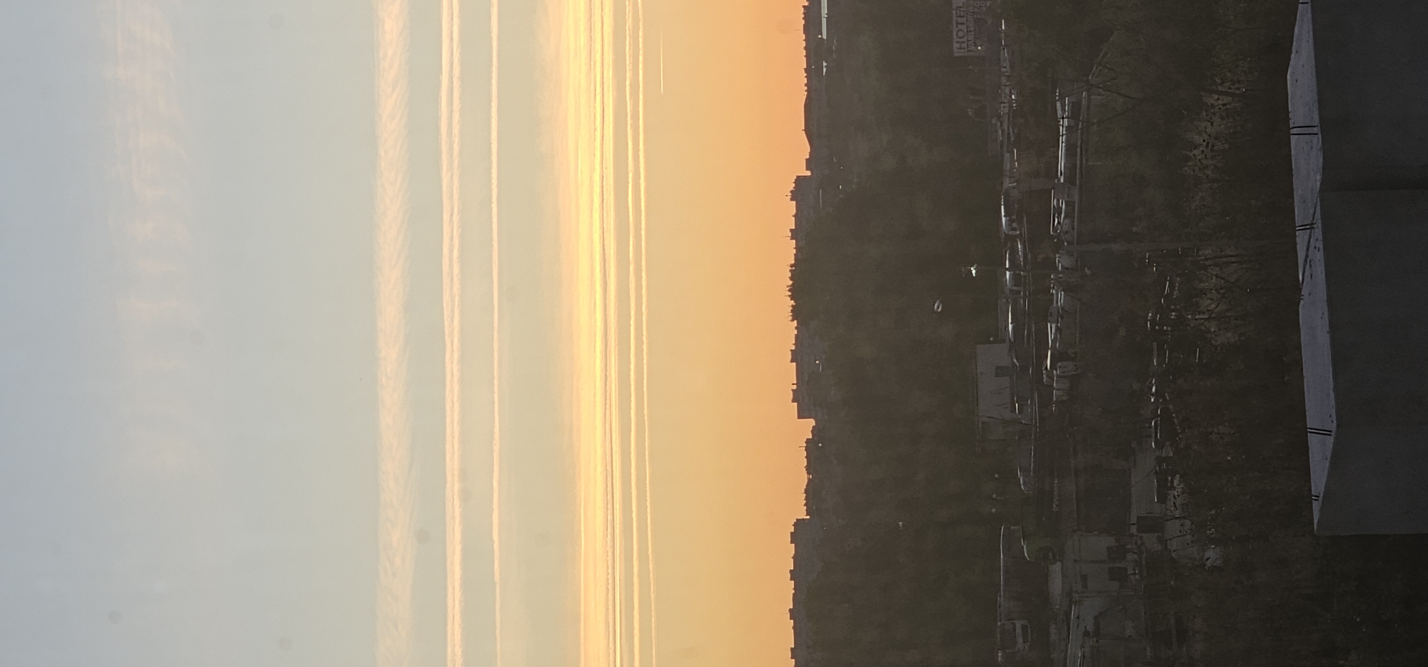 City skyline at dusk, contrails and soft gradients across the sky