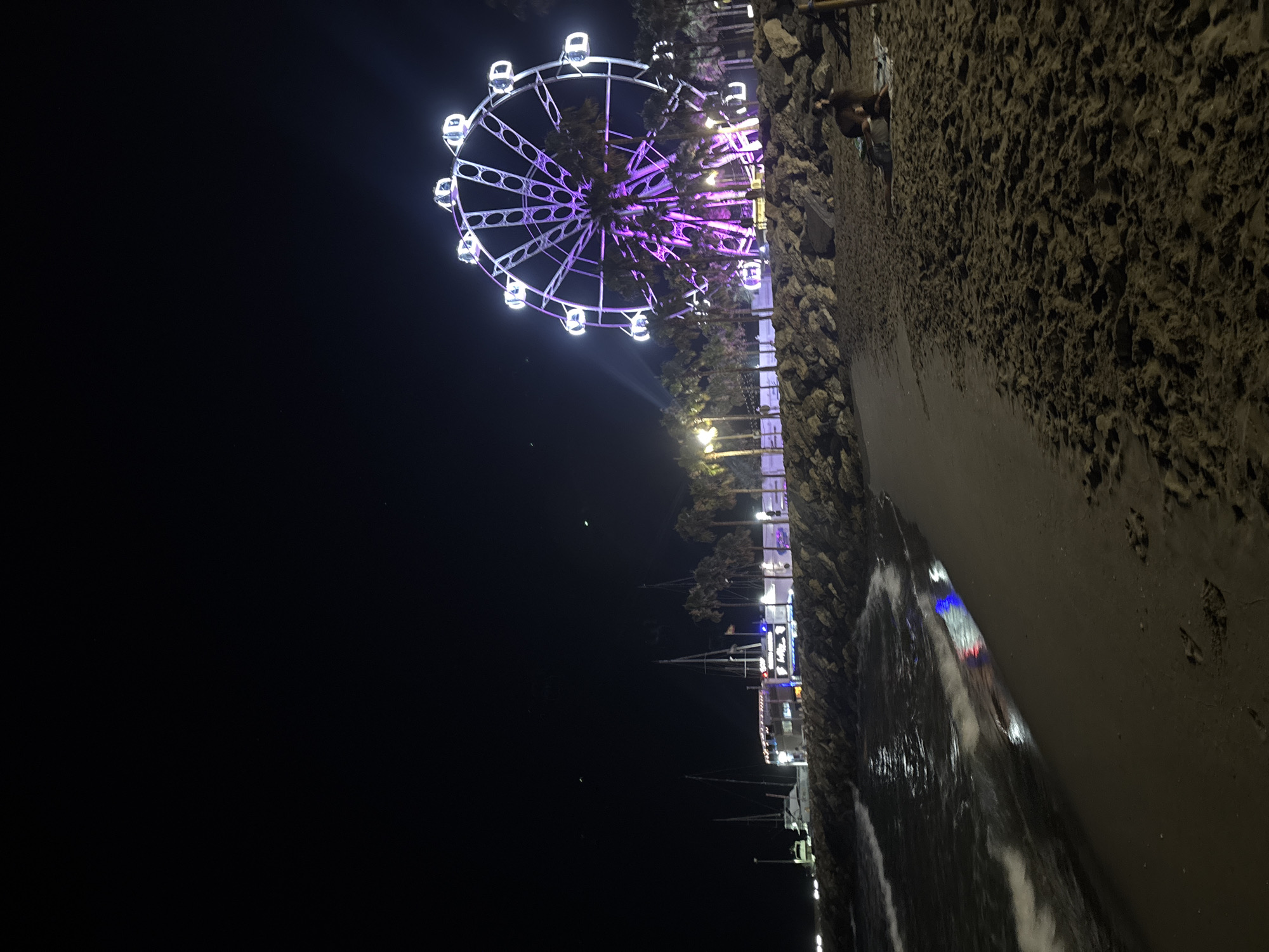 Nighttime beach scene anchored by a glowing Ferris wheel