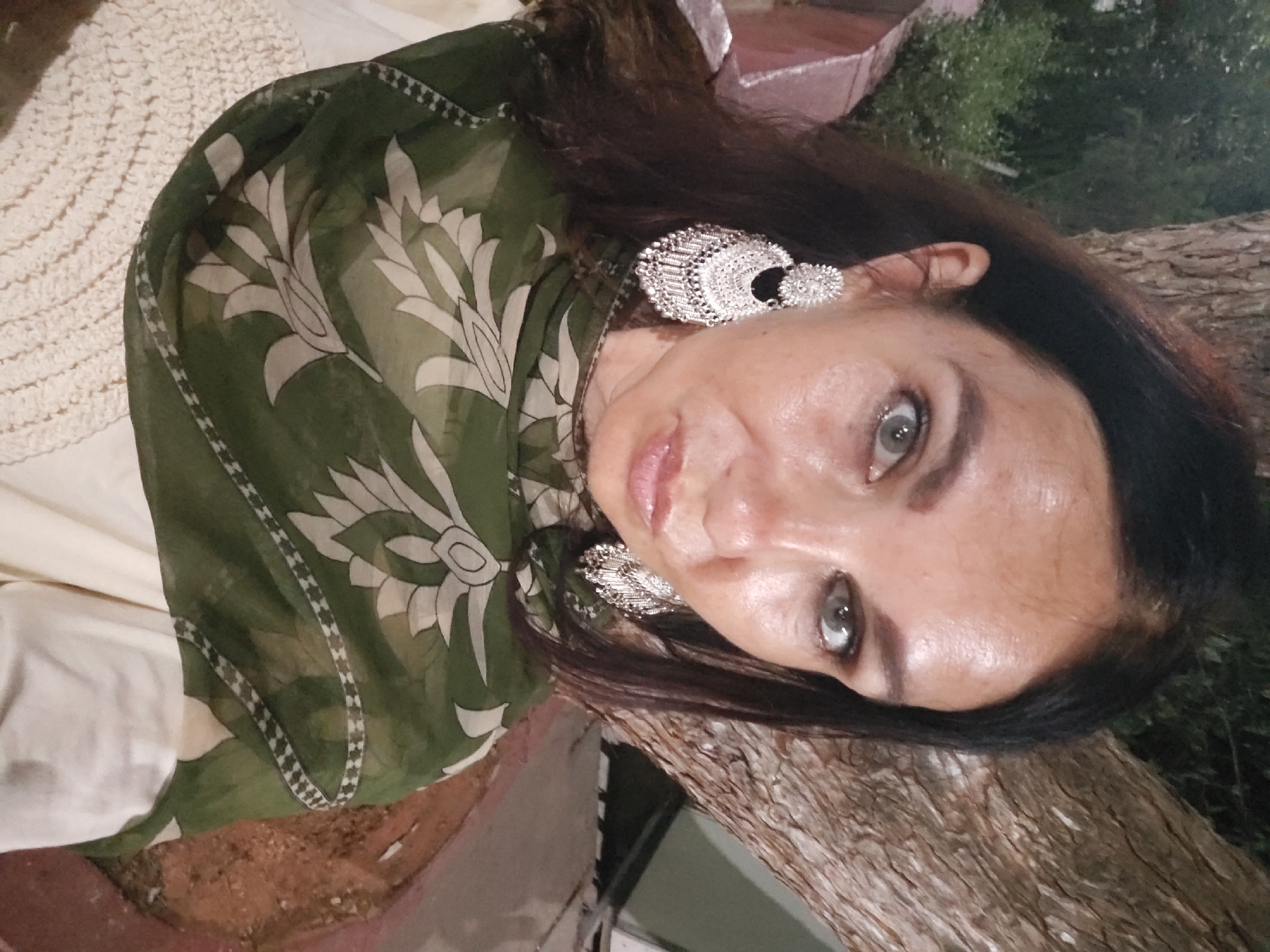 Woman applies makeup, walks among flowering plants in Puttaparthi