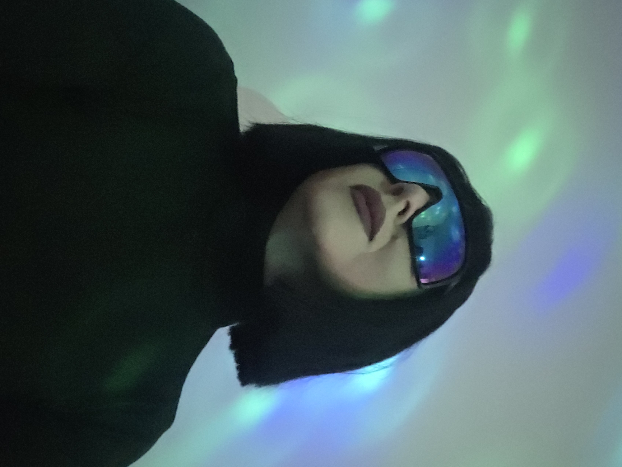 Woman in reflective sunglasses photographed in colorful club lighting