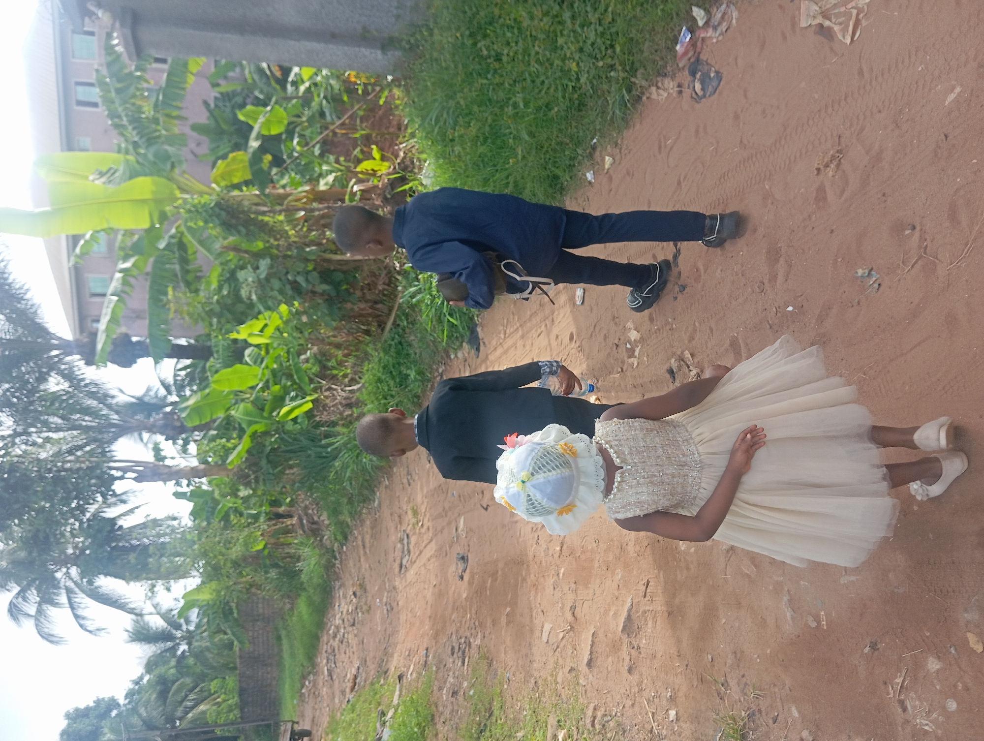Children walk dirt path amid vegetation in Nkpor, Nigeria