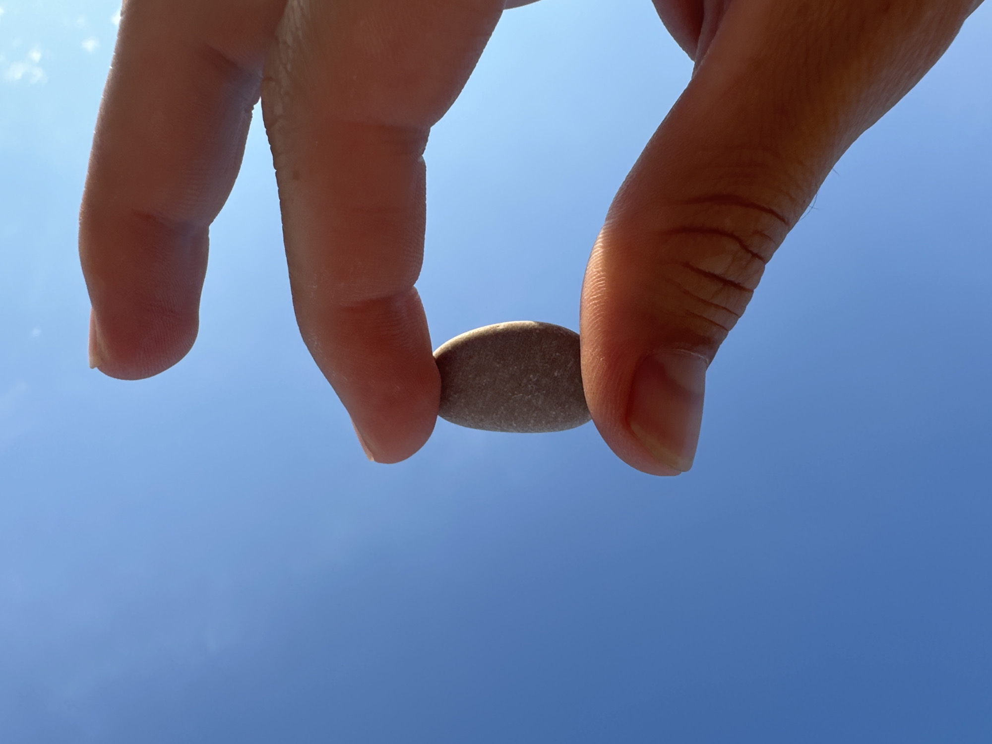 Small gray pebble held up against a clear blue Antalya sky