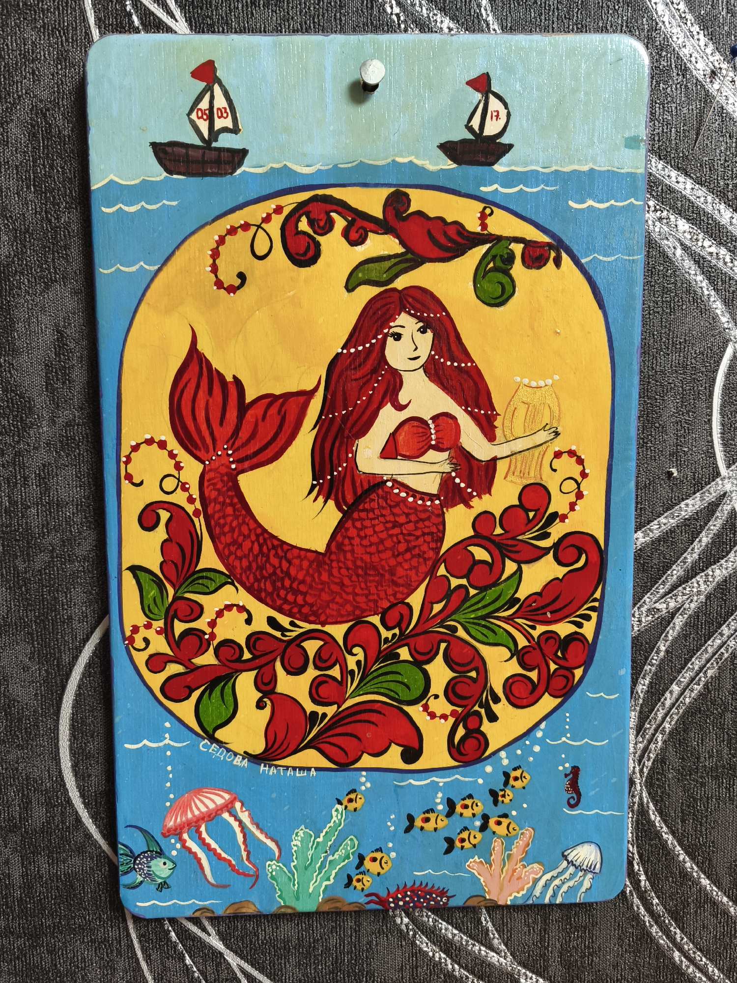 Colorful folk art paintings observed featuring mermaids and village scenes