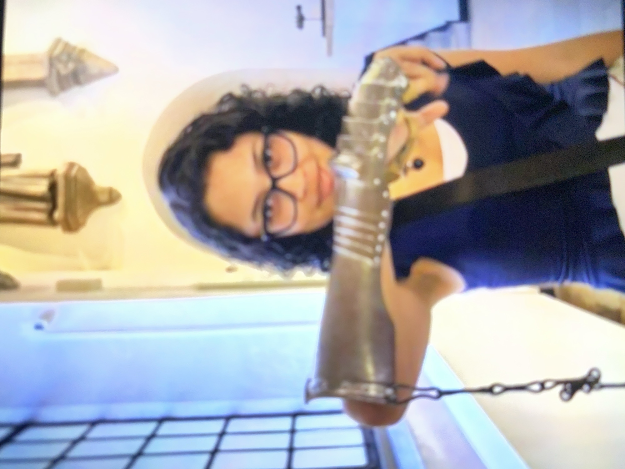 Woman examines medieval gauntlet in ornate interior setting