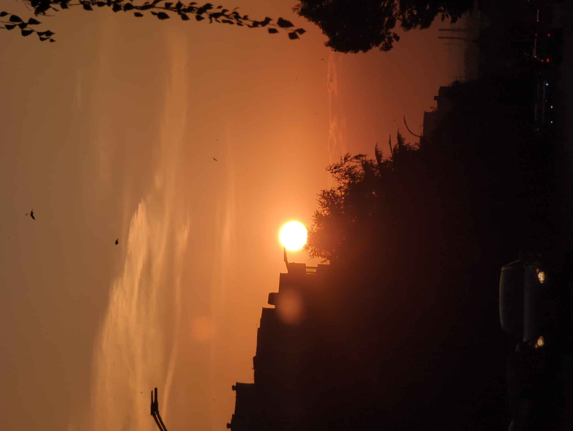 Sunset behind city silhouette with a plane passing through