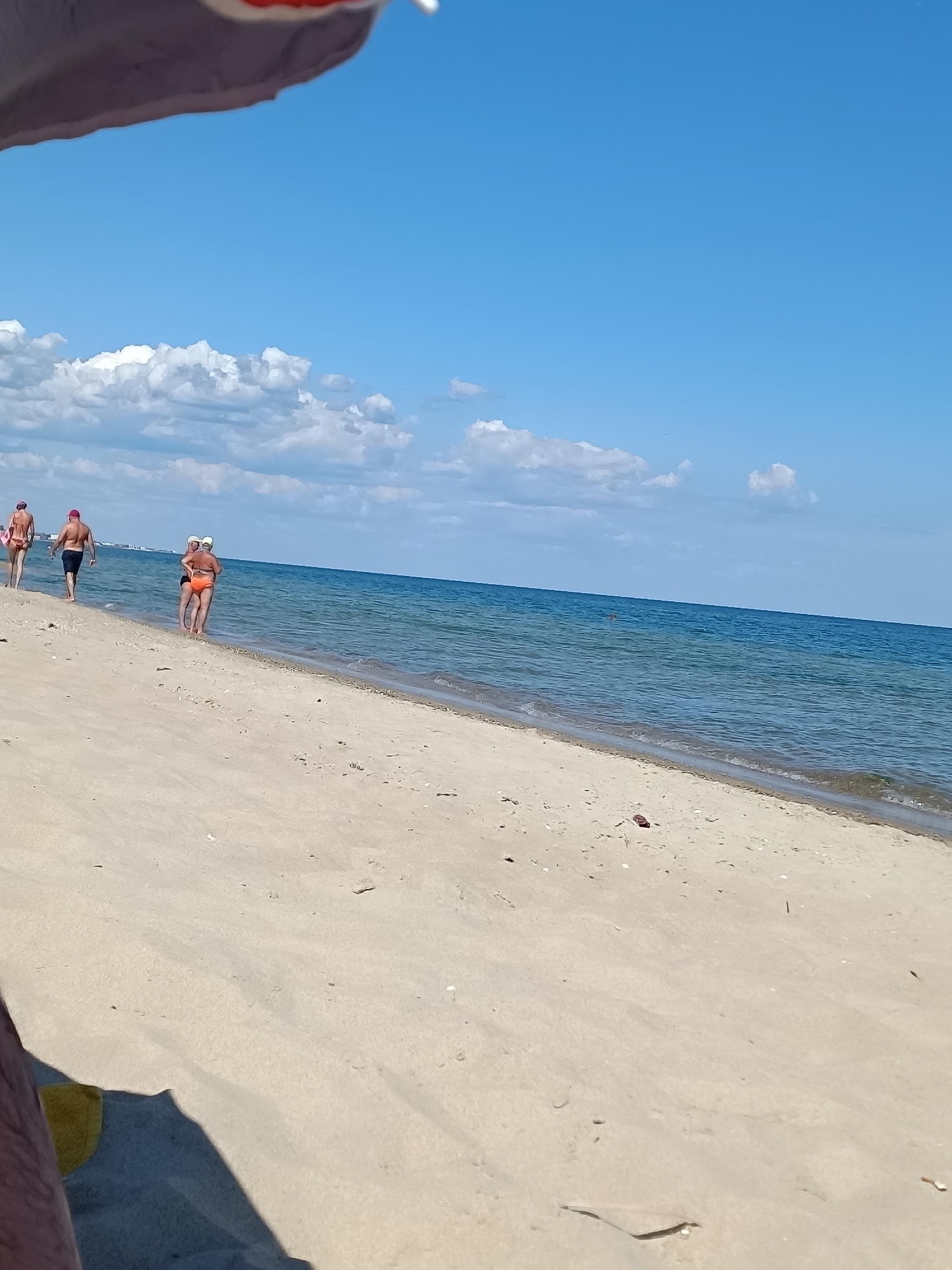 Sunny beach day with crowds, coastline buildings, and a metal tower
