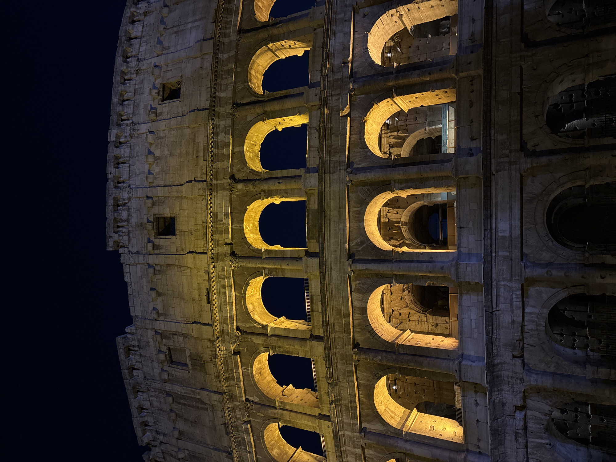 Rome's Colosseum glowing after dark, crowds outside