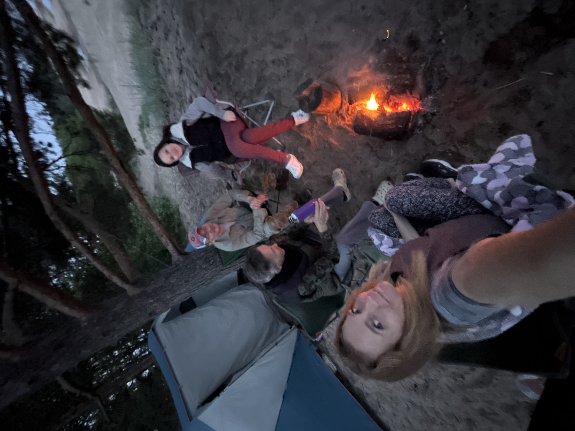 Four adults gather around campfire in Russia at dusk