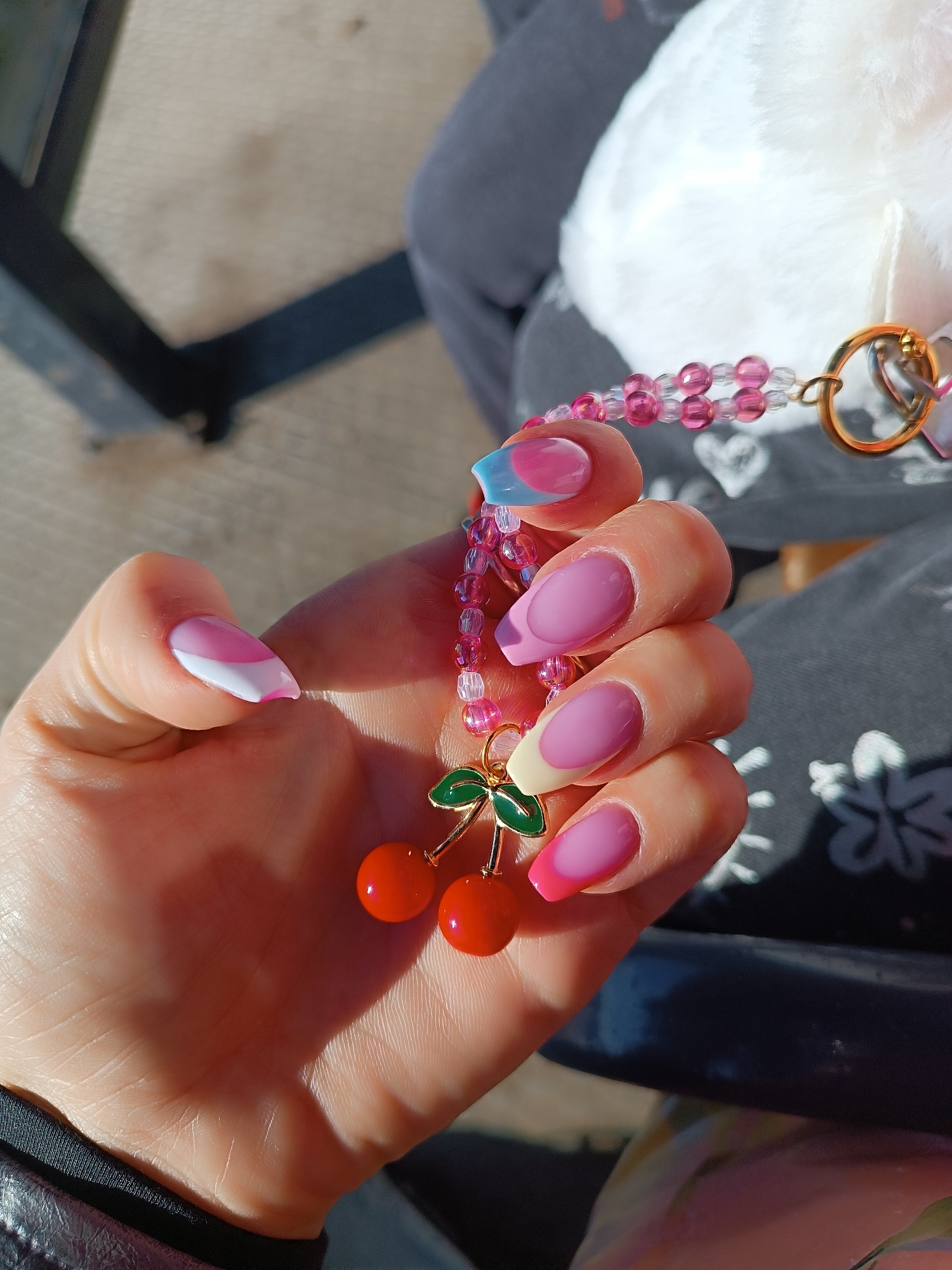 Person displays cherry charm with colorful manicure