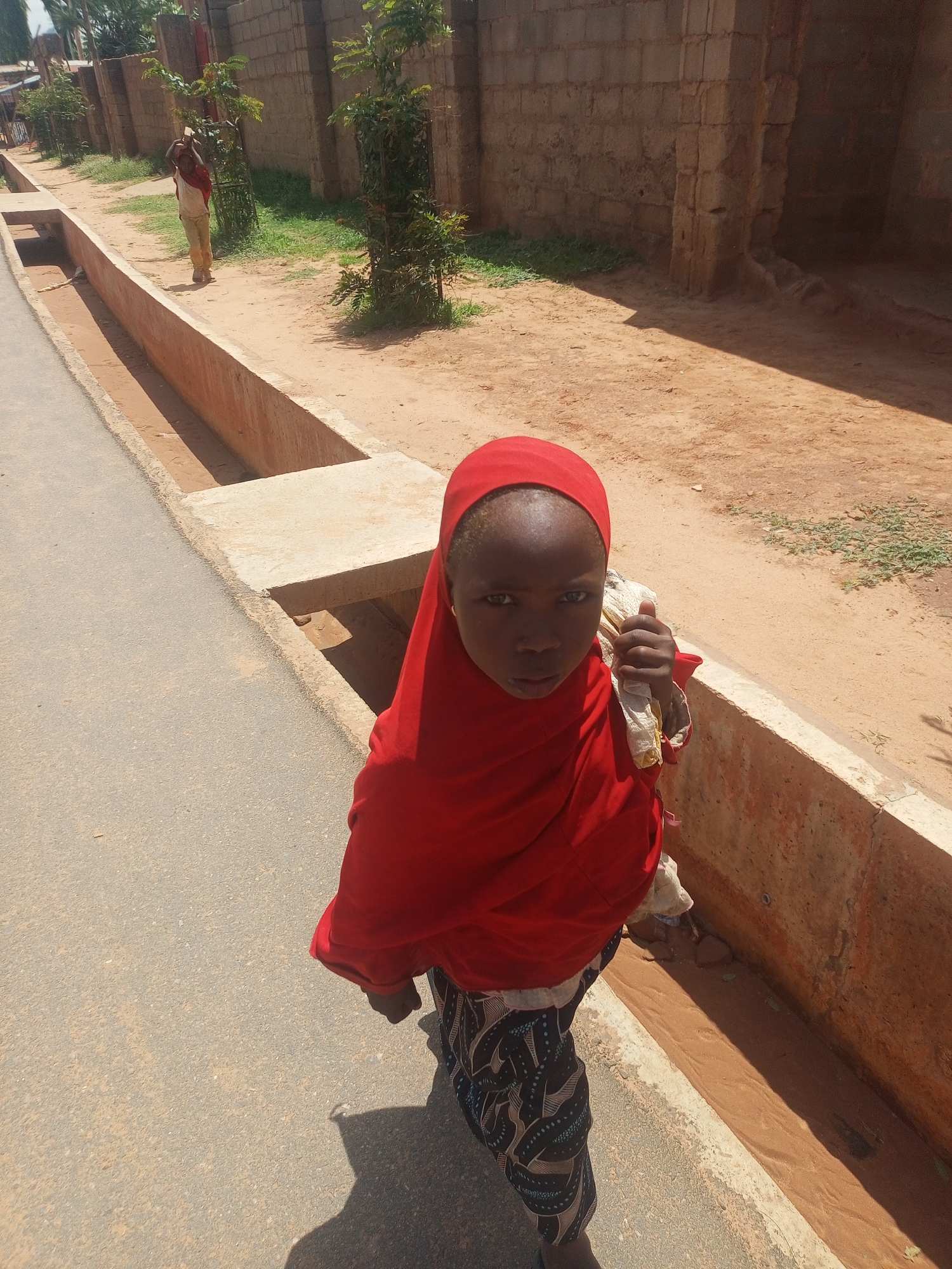 Carrying a white bundle along a street beside a drainage ditch
