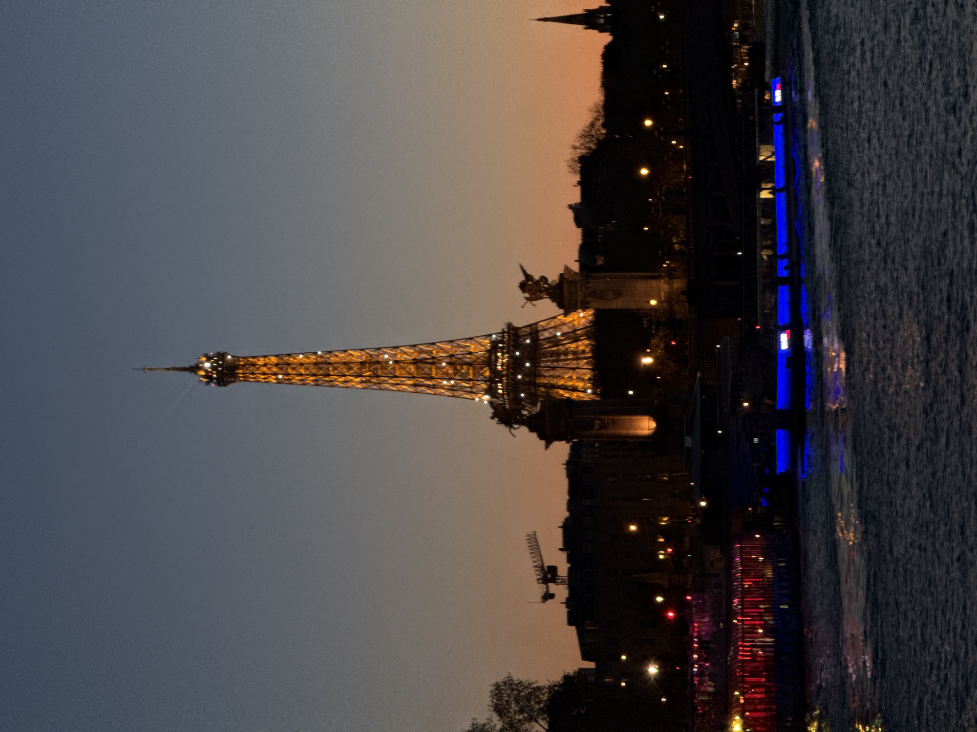 Eiffel Tower glows yellow at dusk over Seine River