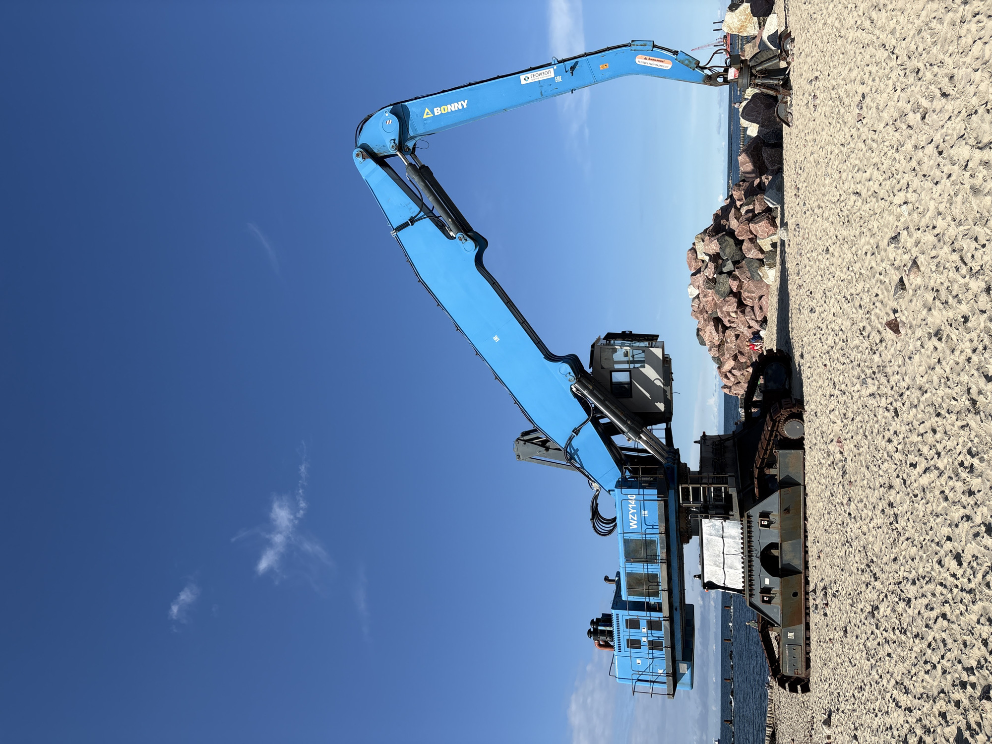 Blue excavator parked on Svetlogorsk beach, arm raised
