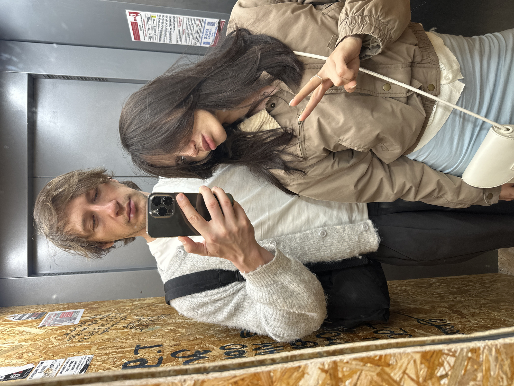 Elevator mirror selfie, casual fits, smartphone in hand.