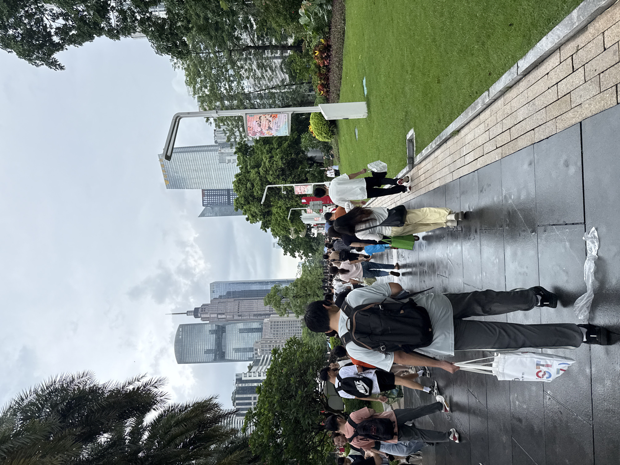 Wet plazas and crowds fill Tianhe's skyscraper district on a cloudy morning.