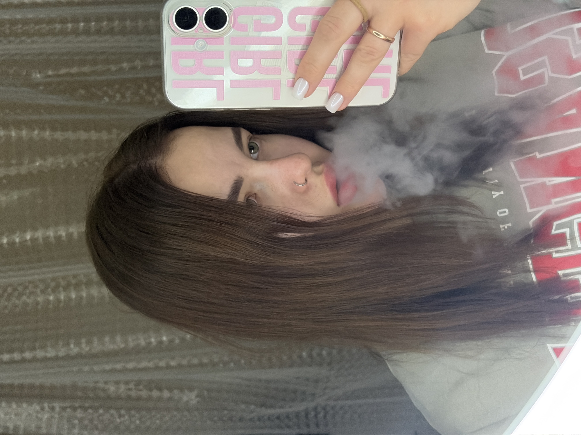 Person with nose ring photographed smoking, holding pink phone case