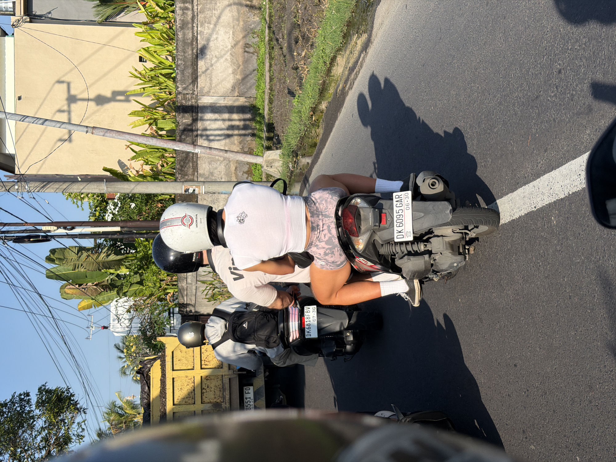 Motorcyclists cruising a tree-lined road in Mengwi, Bali
