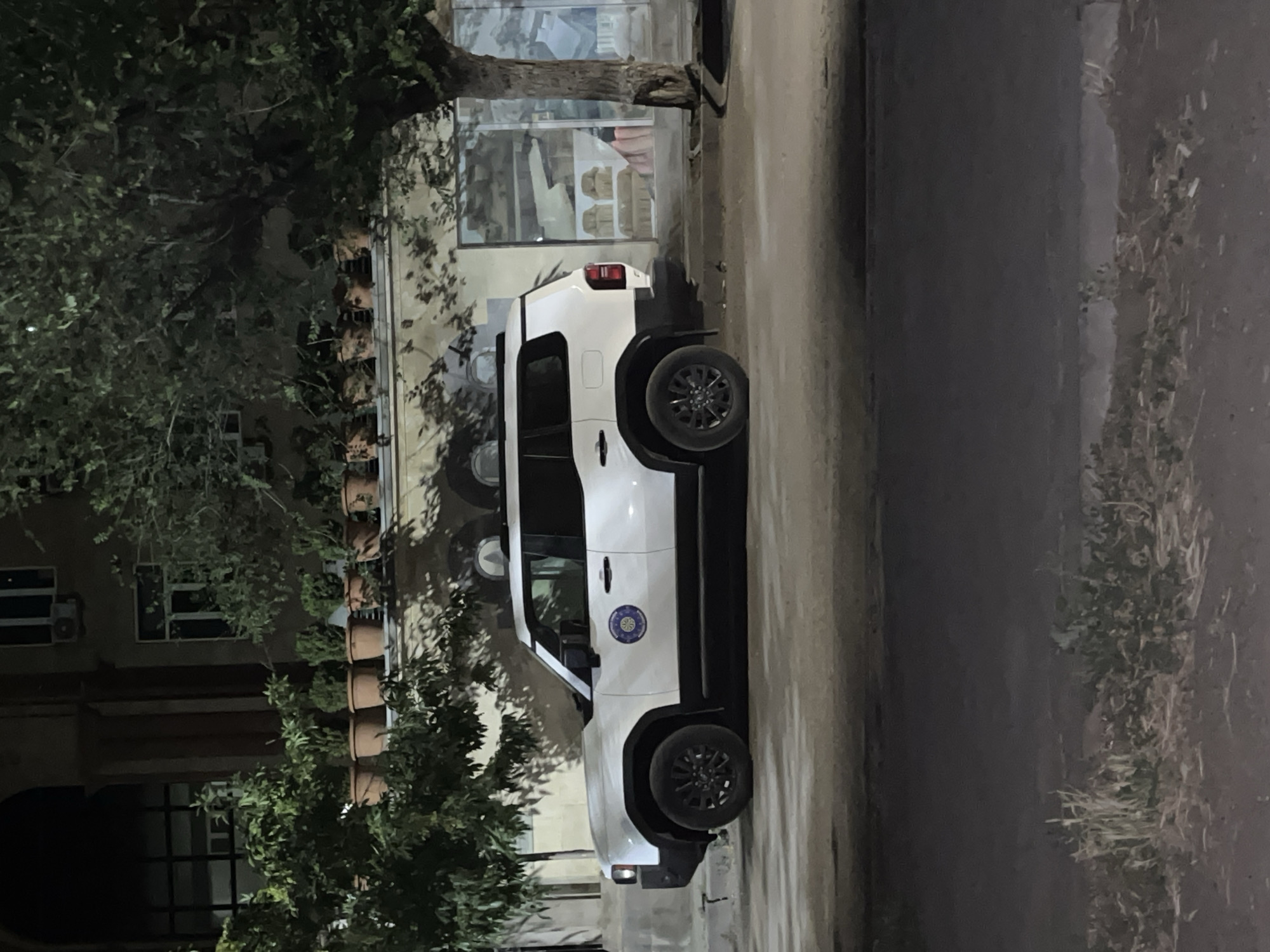 White SUV parked at night outside a building with potted plants