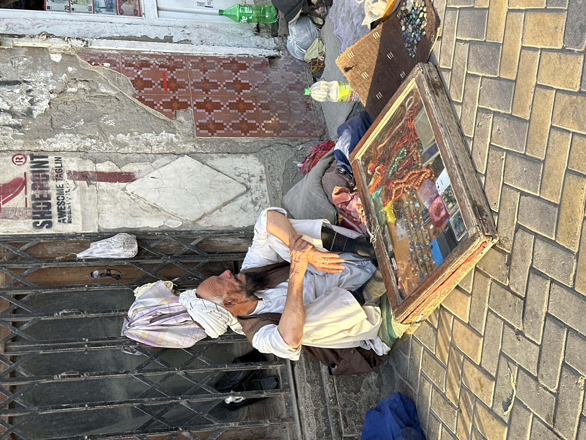 Resting against a metal grate amid belongings in Quetta