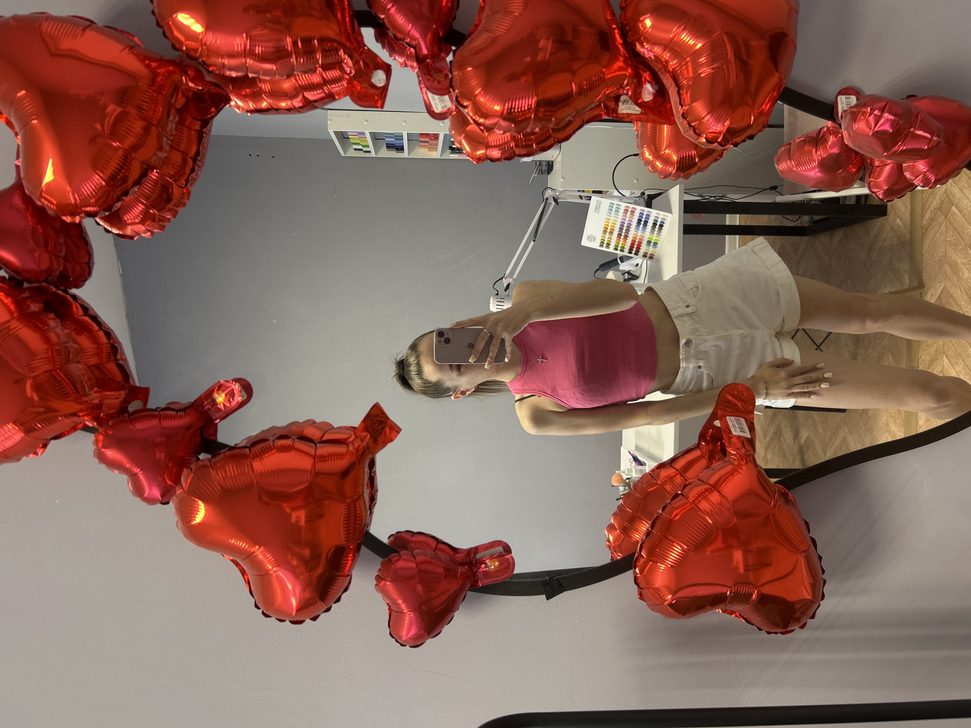 Young woman photographs herself with heart balloons, furniture