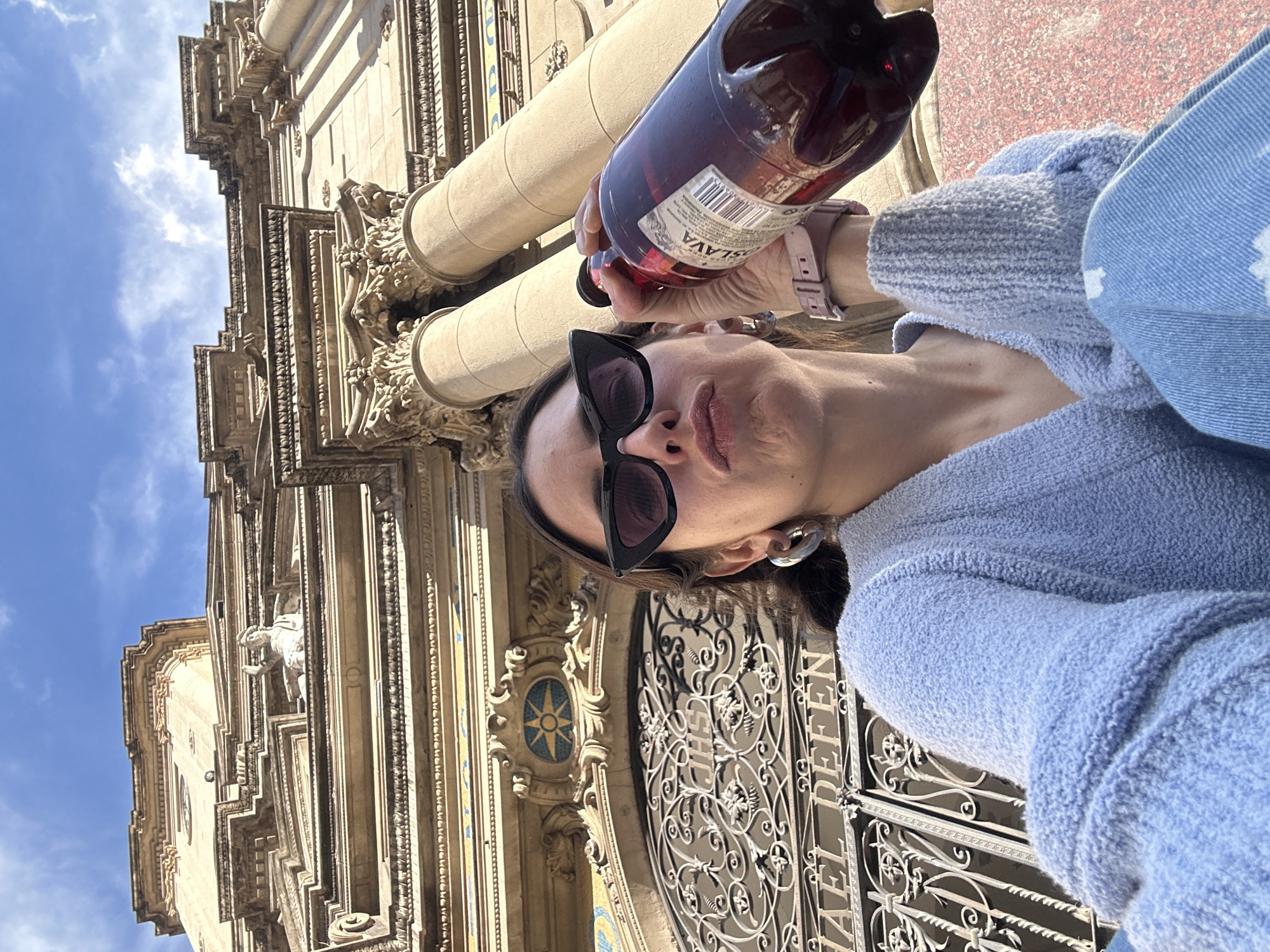 Person takes selfie with red bottle near ornate Buenos Aires building