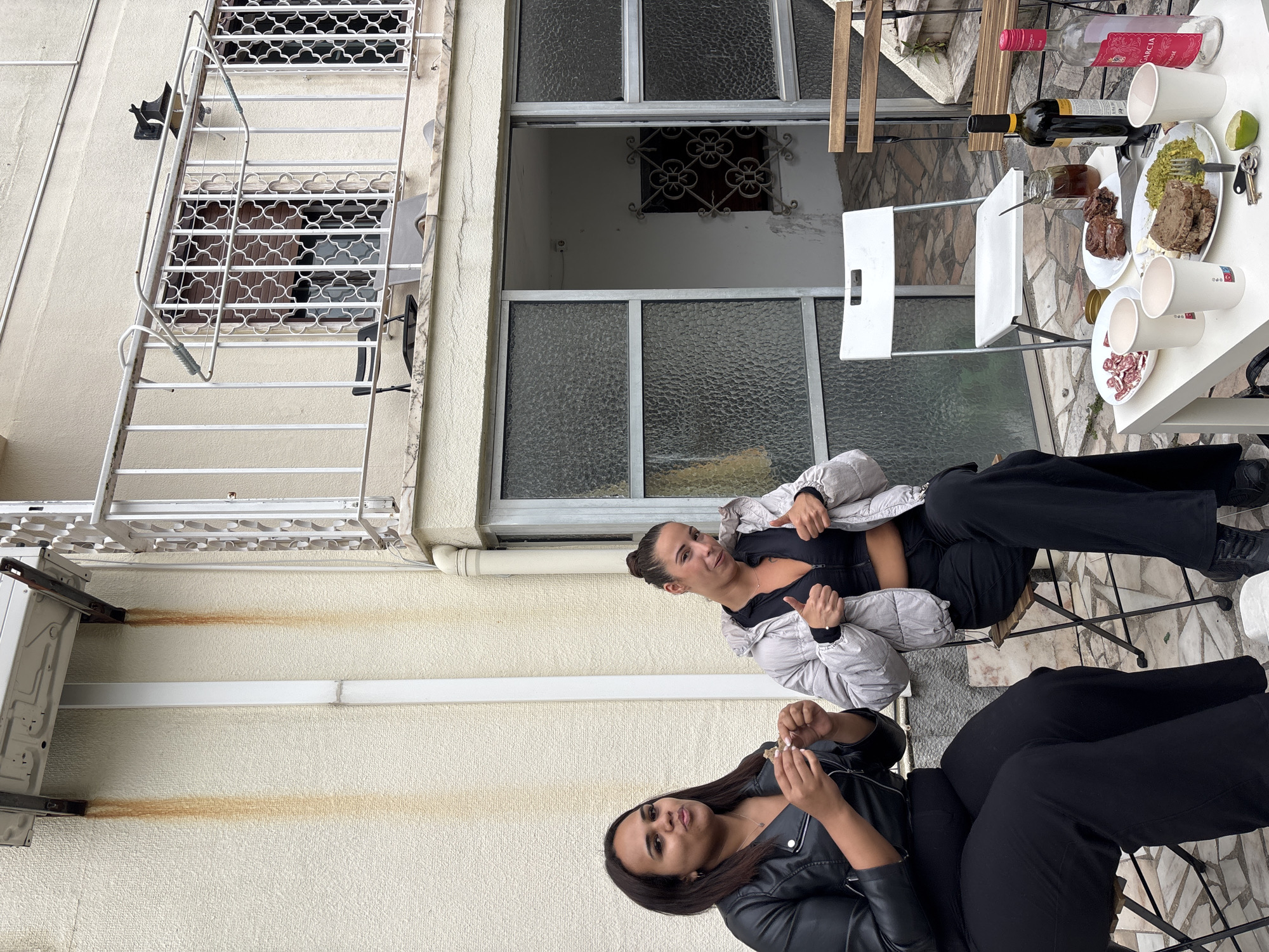 Two women gather on Lisbon balcony under overcast skies