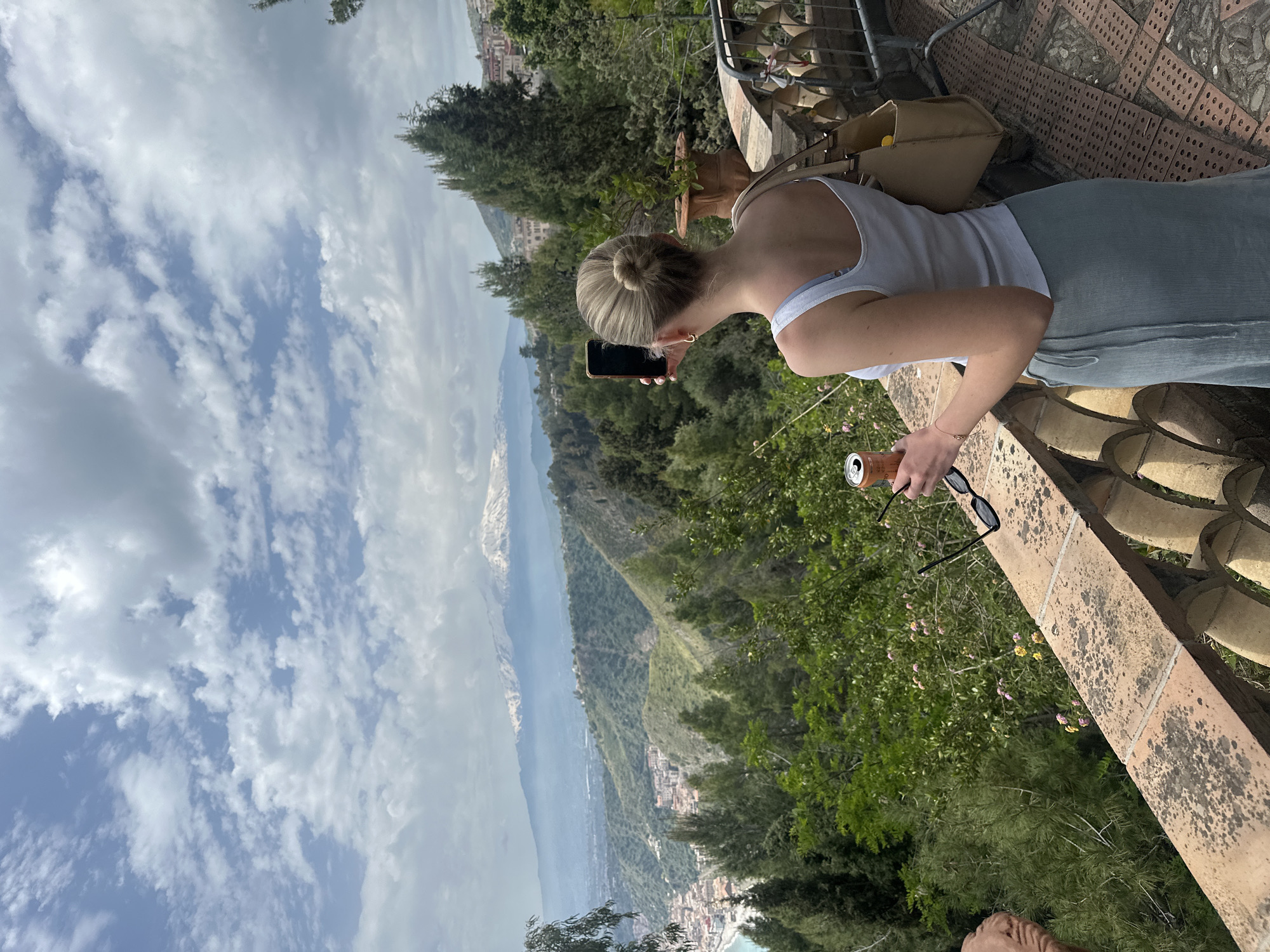 Woman enjoys scenic Taormina balcony view with mobile device
