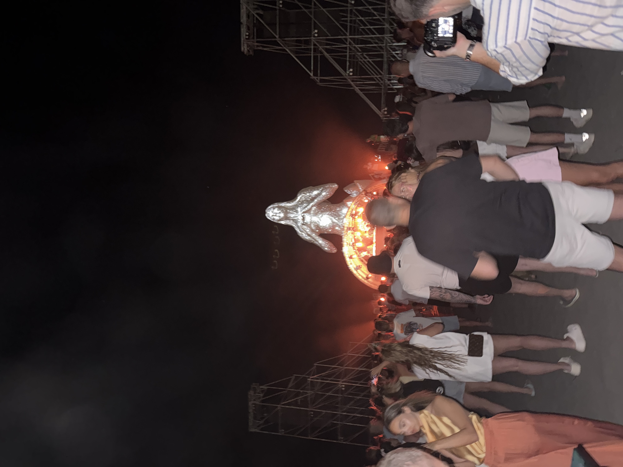 Night crowd gathers around glowing metallic statue at outdoor event