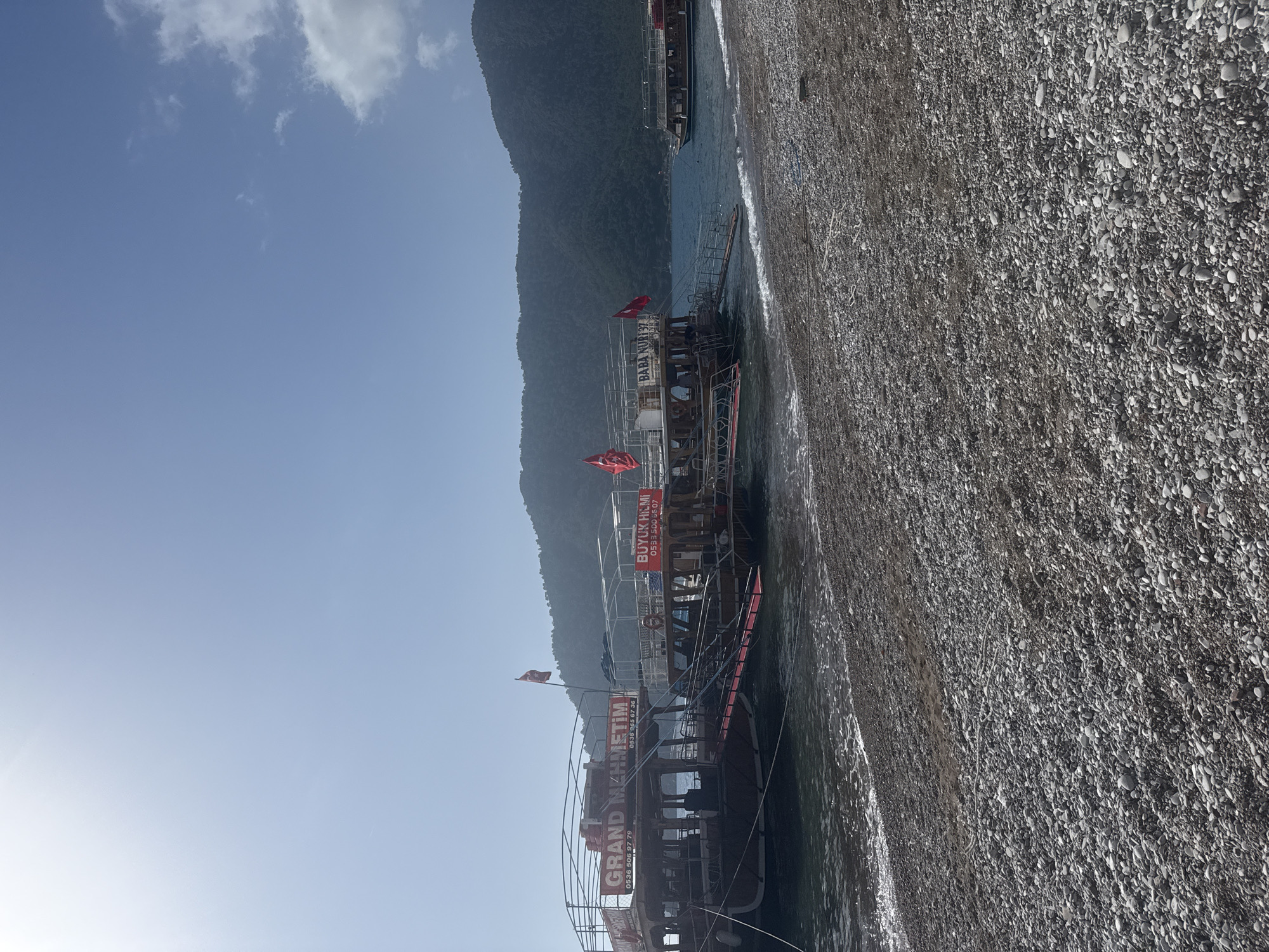Tour boats dock at Kumluca beach as morning visitors gather