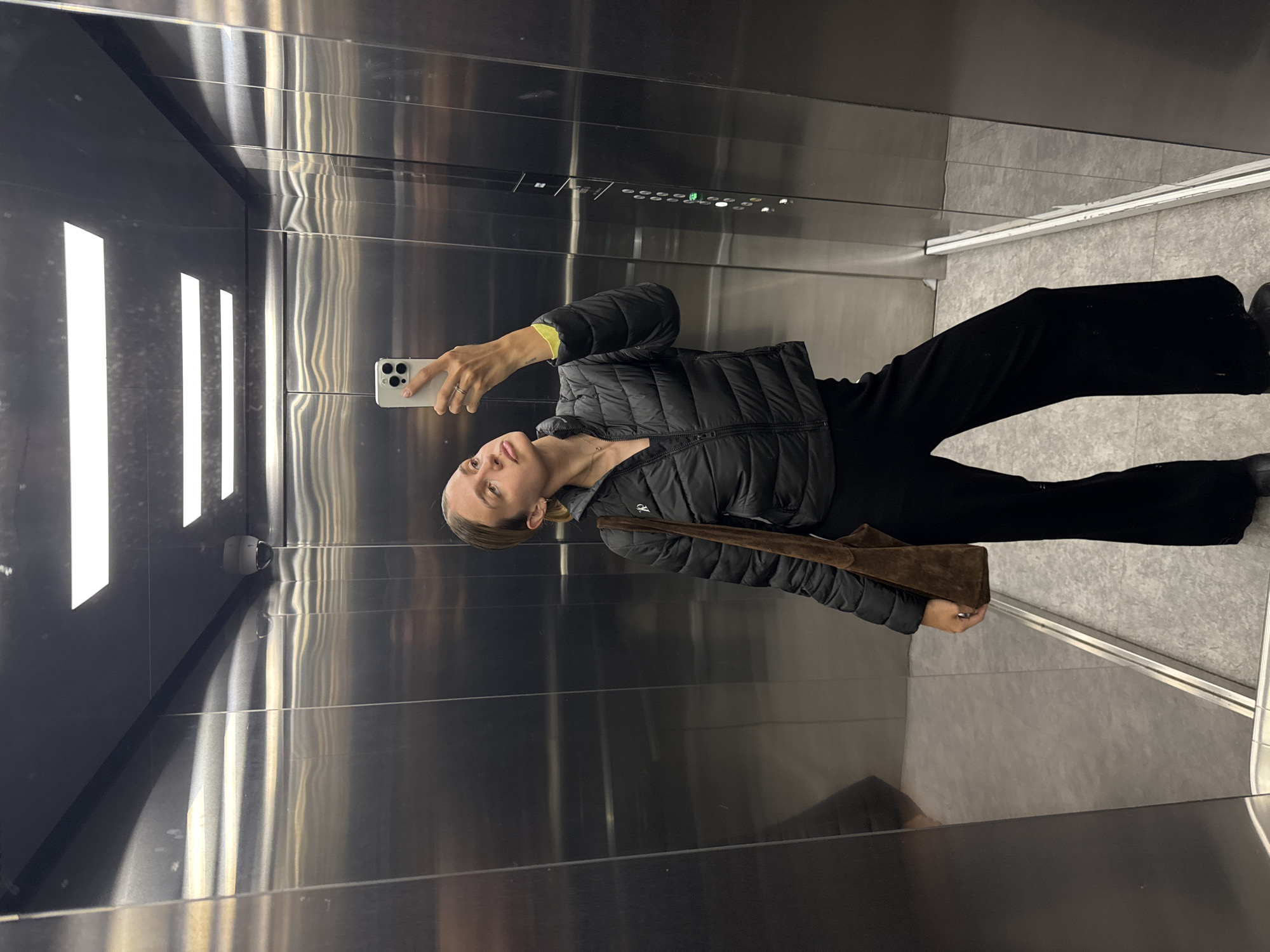 Woman takes selfie in elevator wearing black outfit