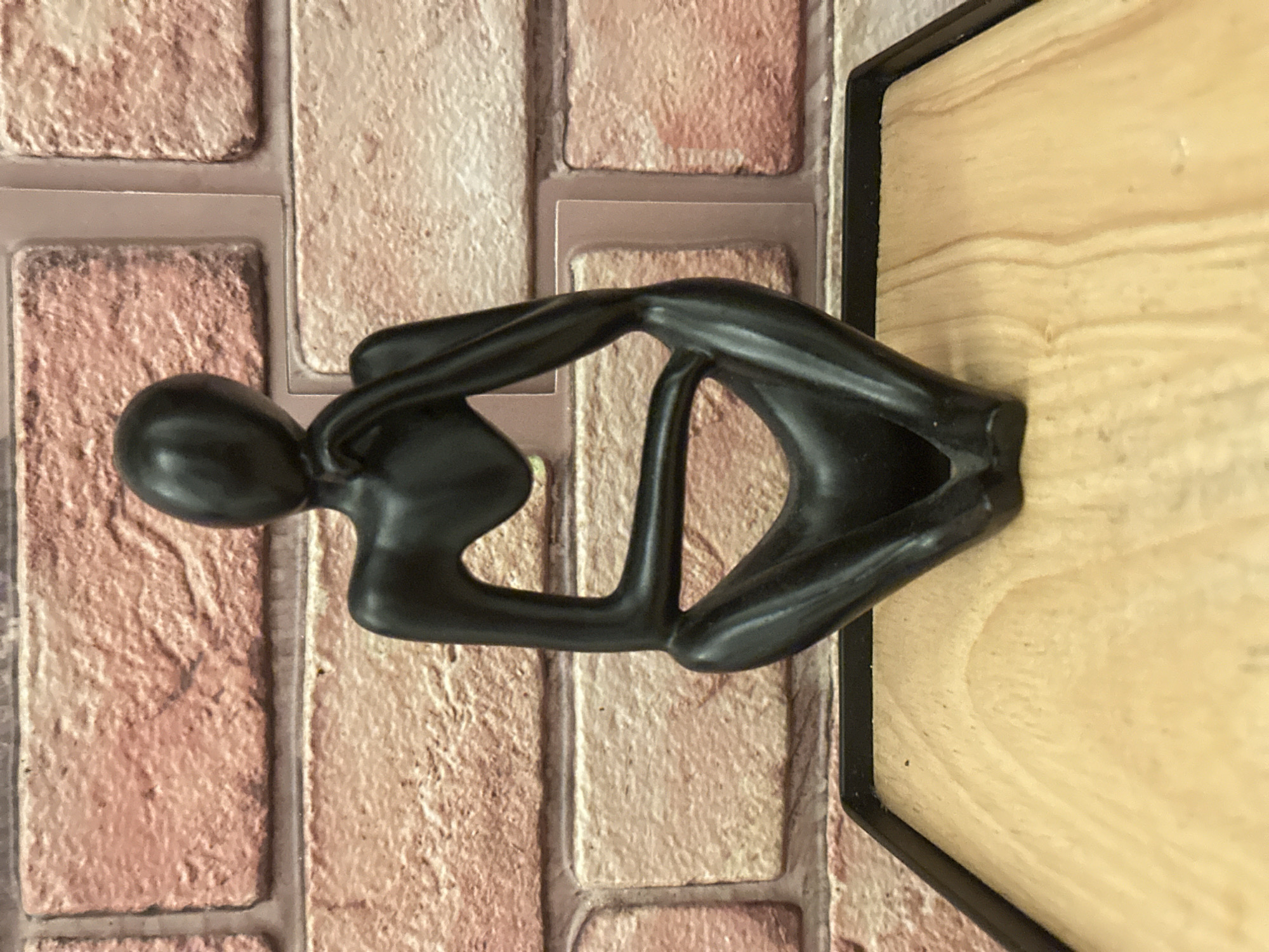 Black contemplative sculpture observed on London brick wall display