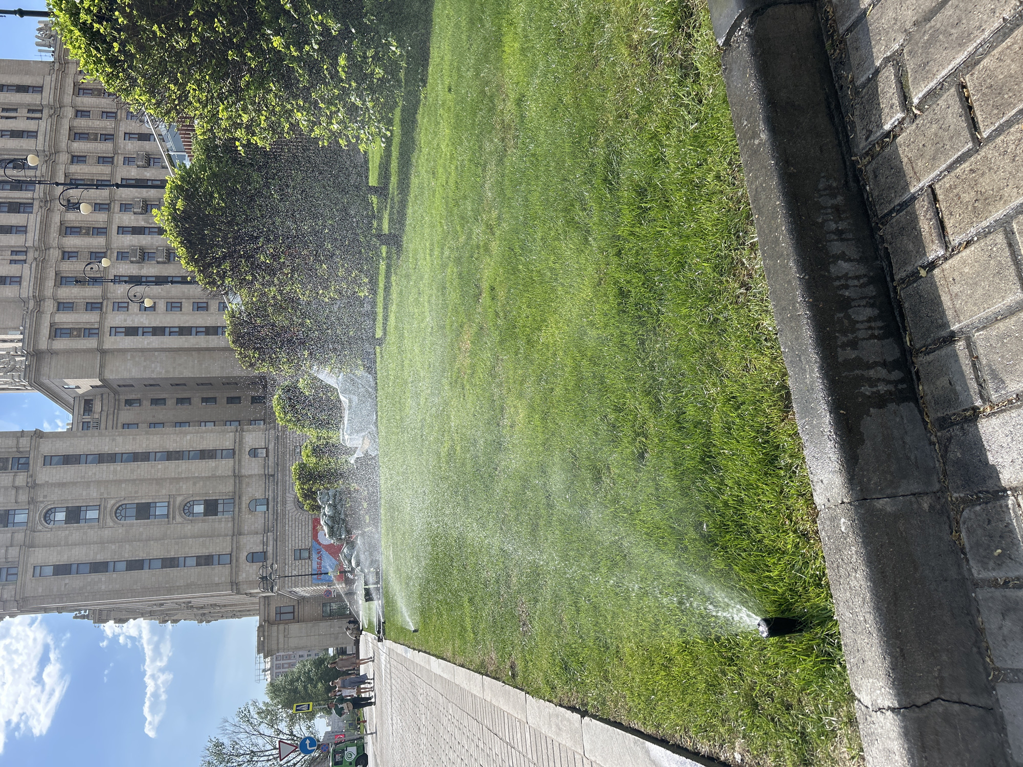 Urban lawn sprinklers create rainbow effects in afternoon sunlight