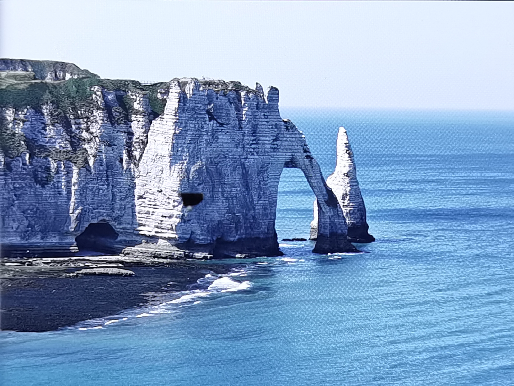 Chalk cliffs, a lone windsurfer, and beached boats on a quiet coast