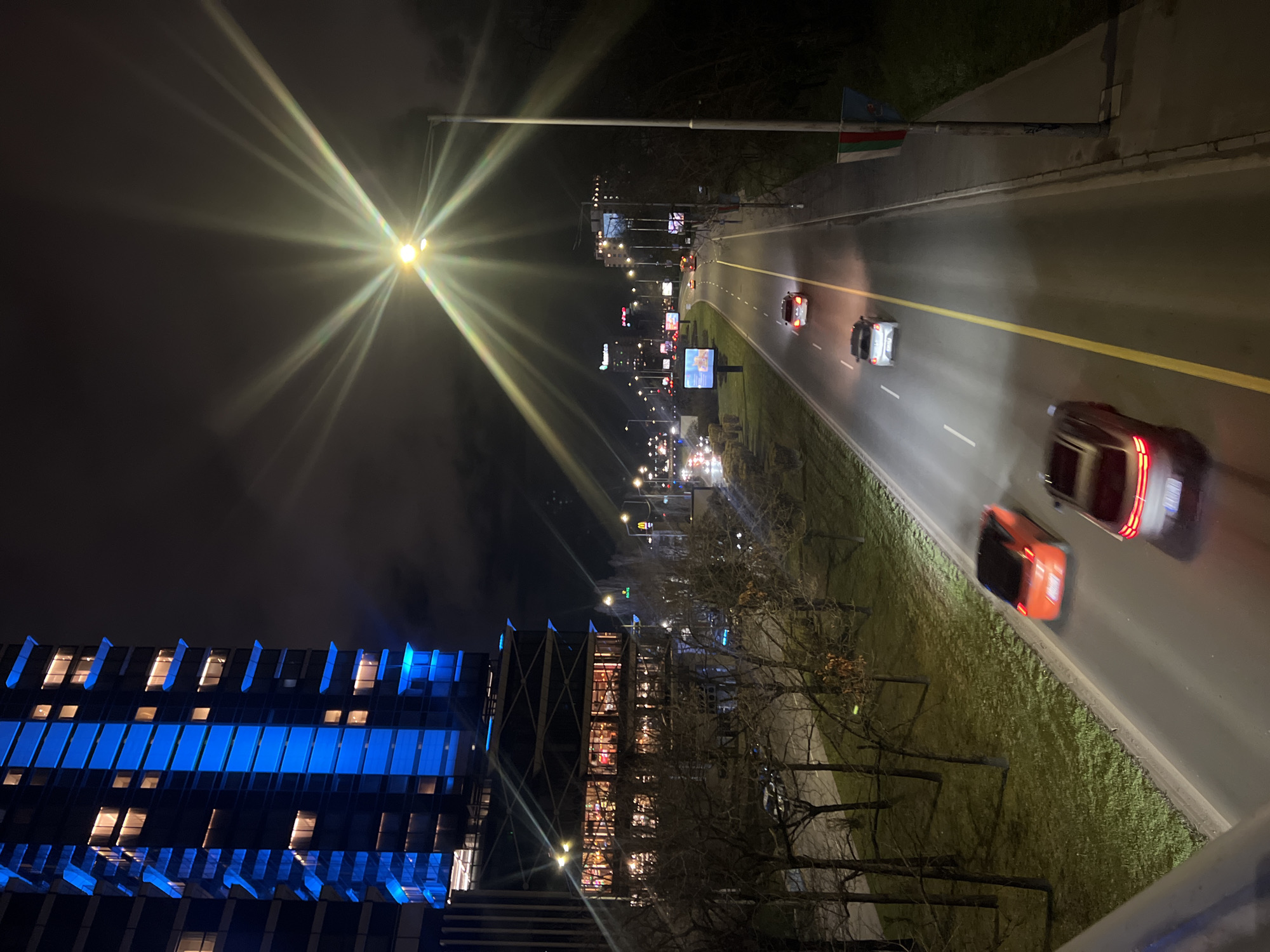 Evening traffic flows past blue-lit buildings in Sofia