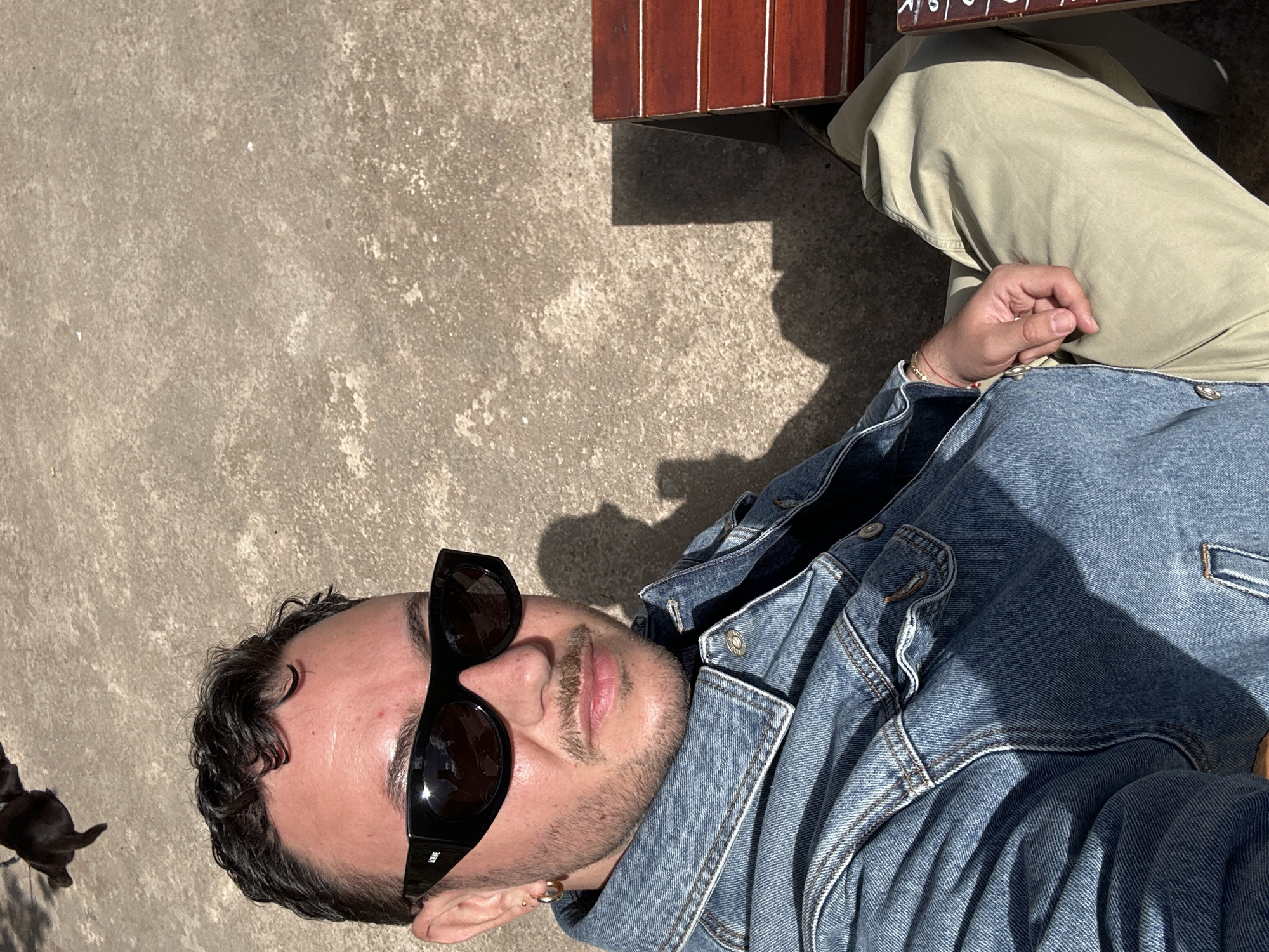 Person in sunglasses and denim jacket sits by bench in Madrid